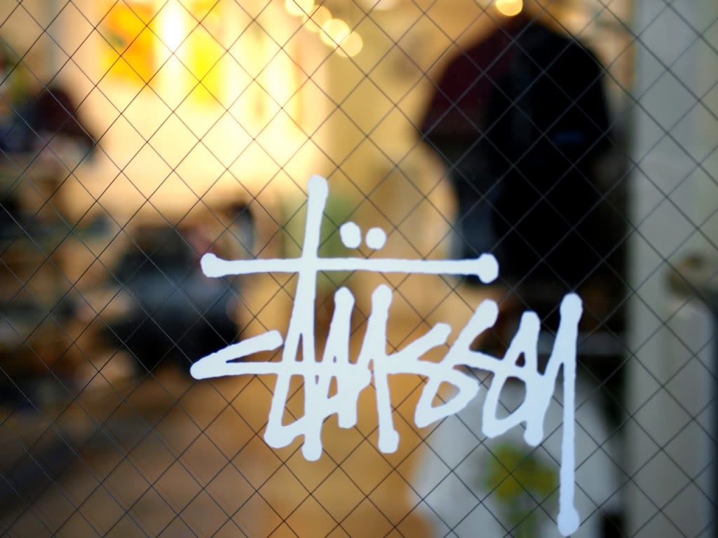 Stussy logo displayed on a glass storefront, hinting at the brand's presence within
