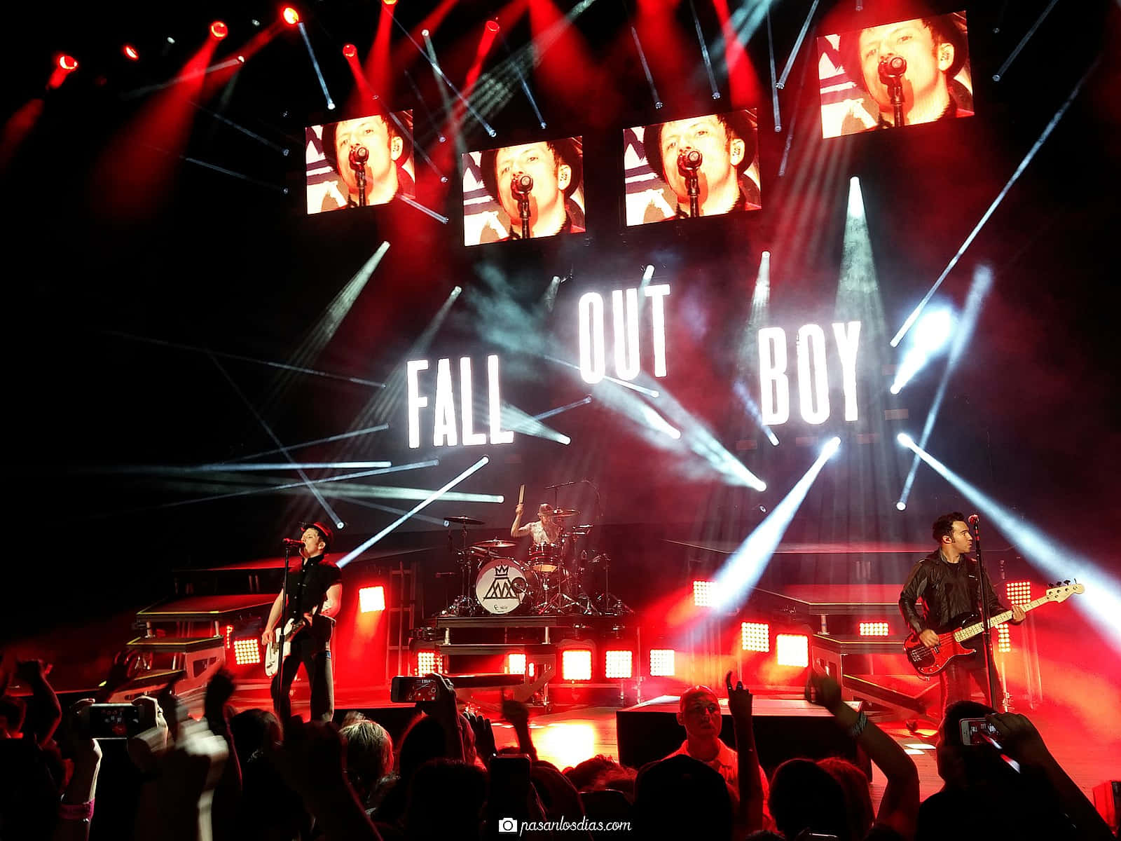 Fall Out Boy performing live on stage with vibrant red lighting and screens displaying close-ups of the lead singer