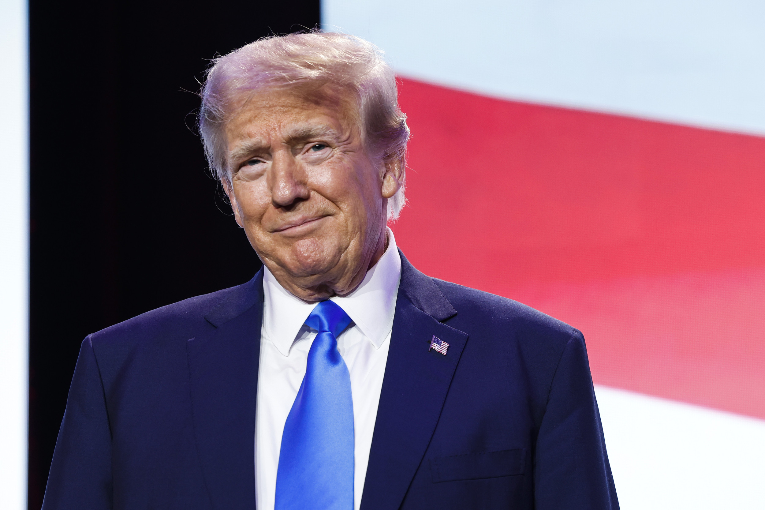 Donald Trump, wearing a suit and tie, smiles slightly at a 2024 campaign event