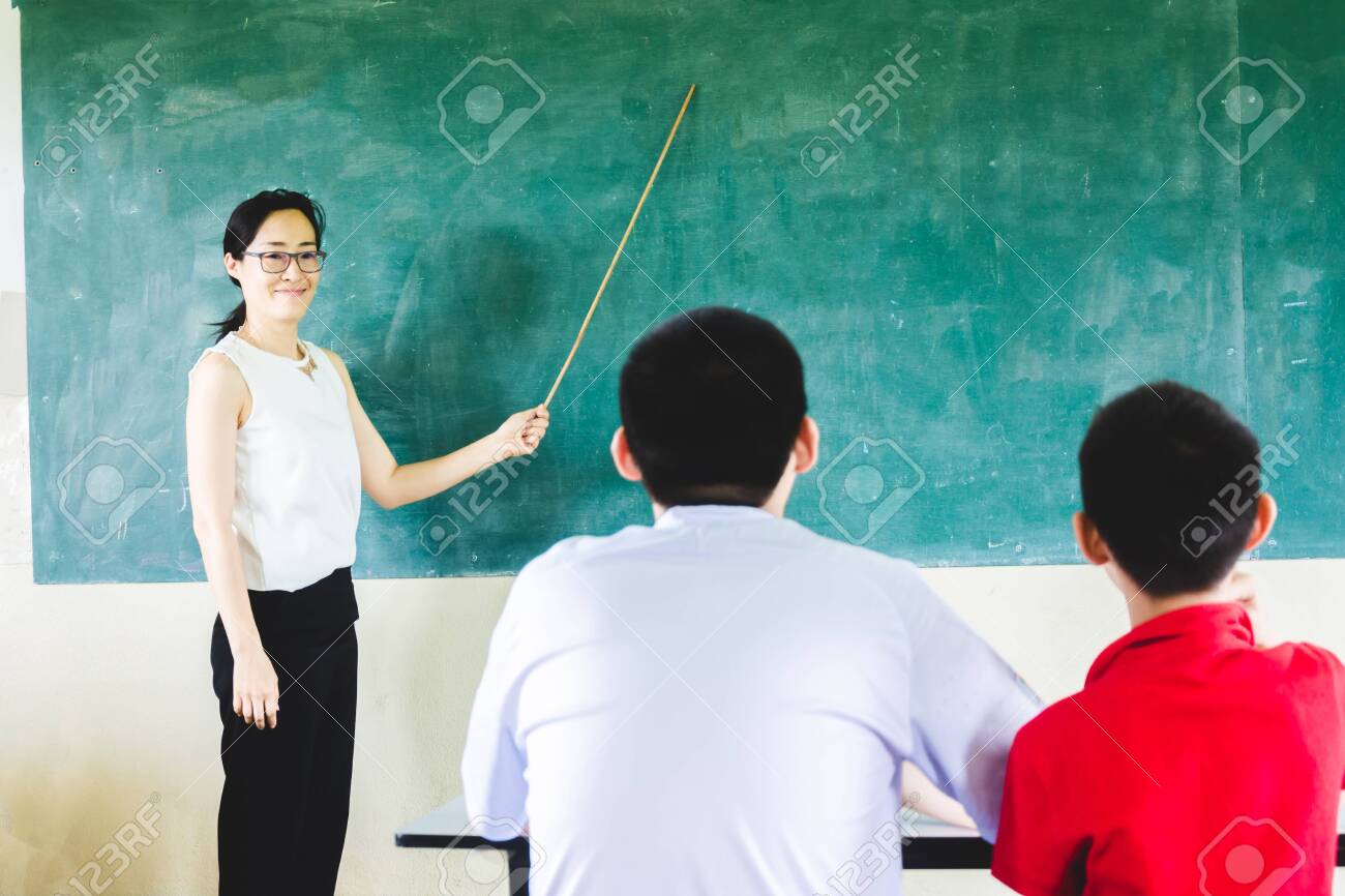 Asian Teacher Teaching In Classroom With Cholkboard Background