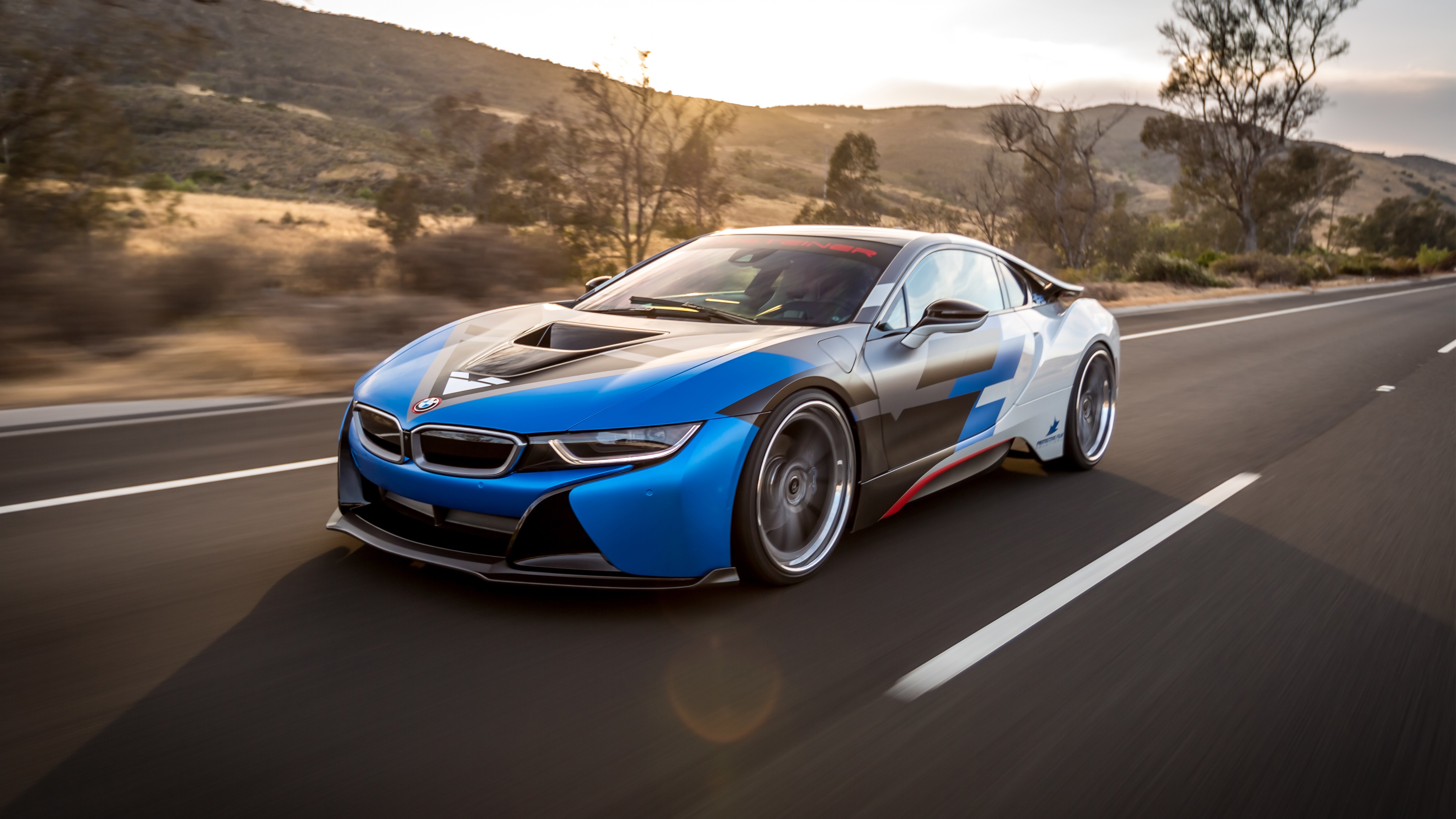 A customized BMW i8 sports car driving on a scenic highway