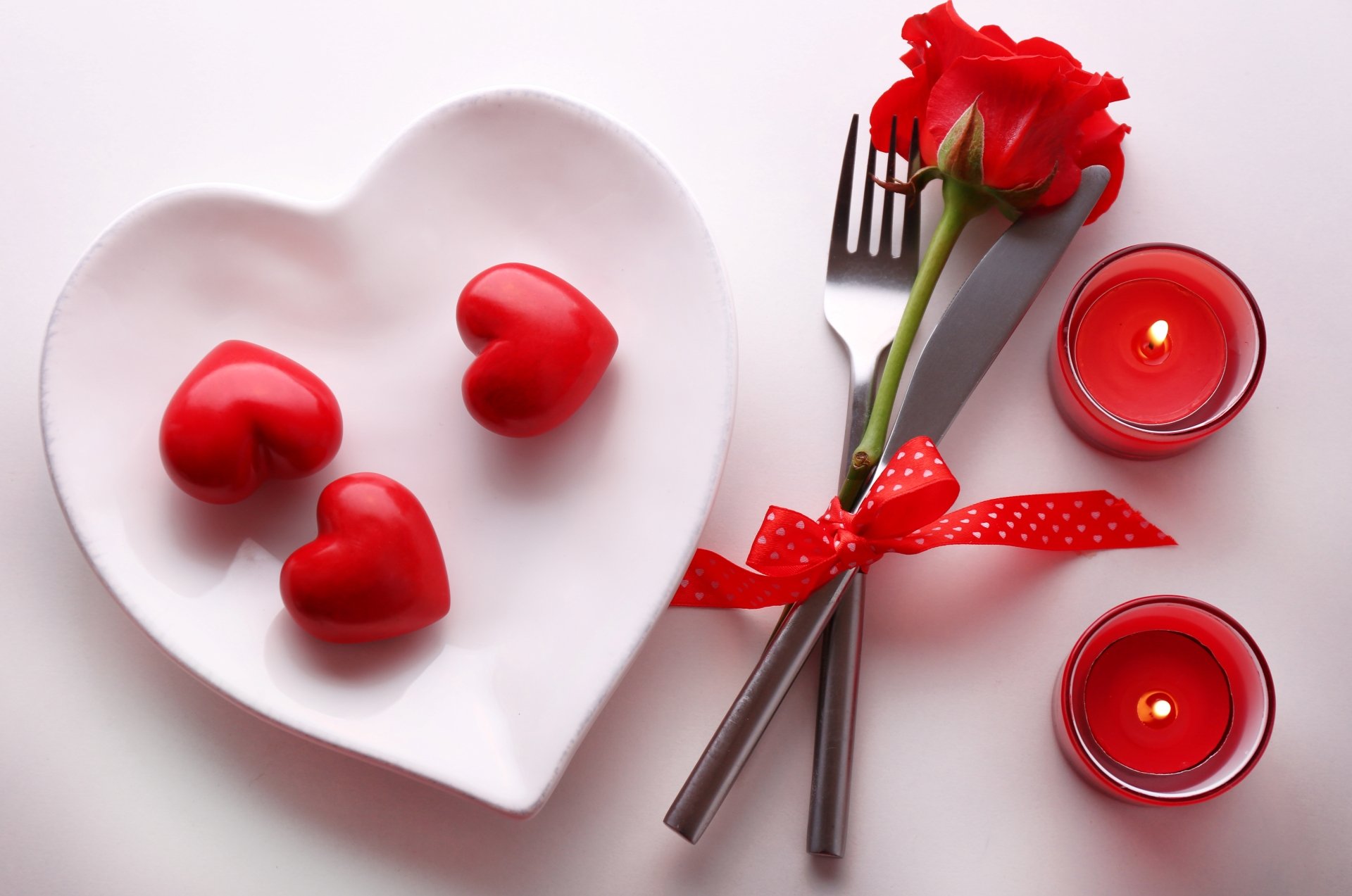 Romantic Valentine's Day table setting with heart-shaped plate, red candles, rose, and cutlery