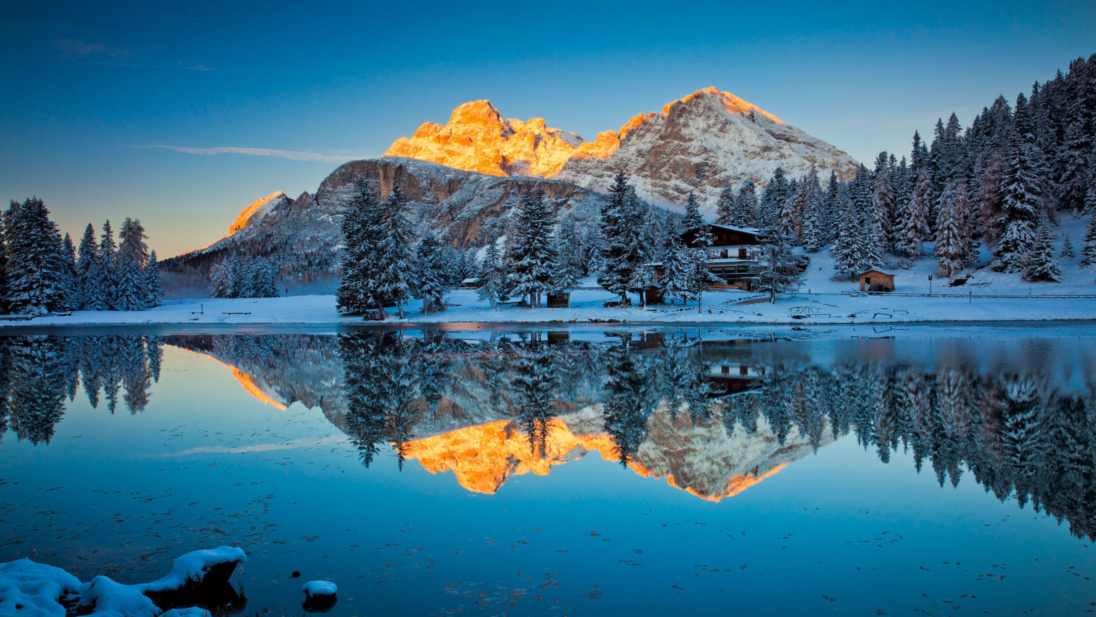 Stunning 4K winter landscape with snow-covered mountains reflecting in a crystal-clear lake at sunrise