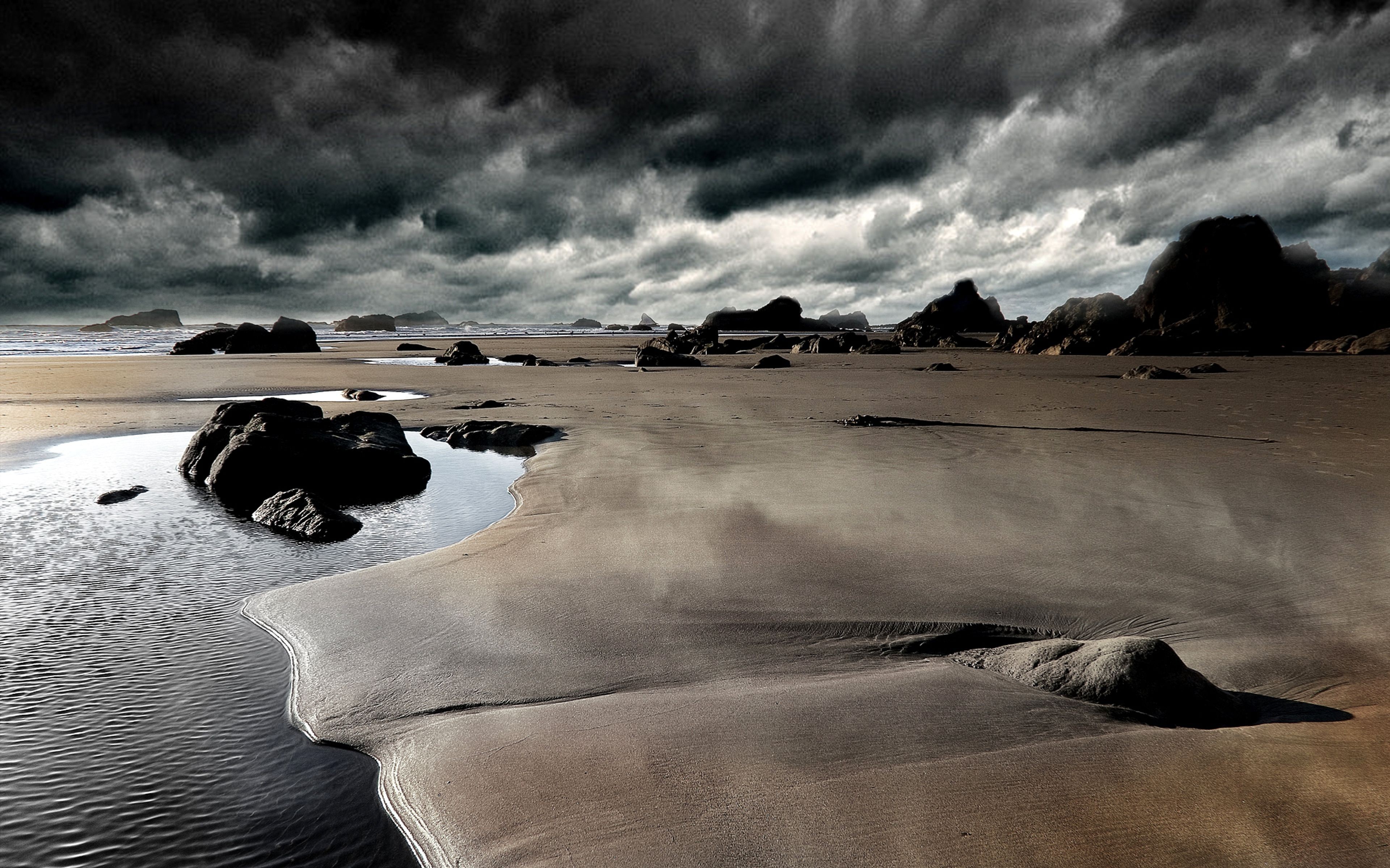 Dramatic coastal landscape with dark, stormy clouds, sandy beach, and rocky outcrops