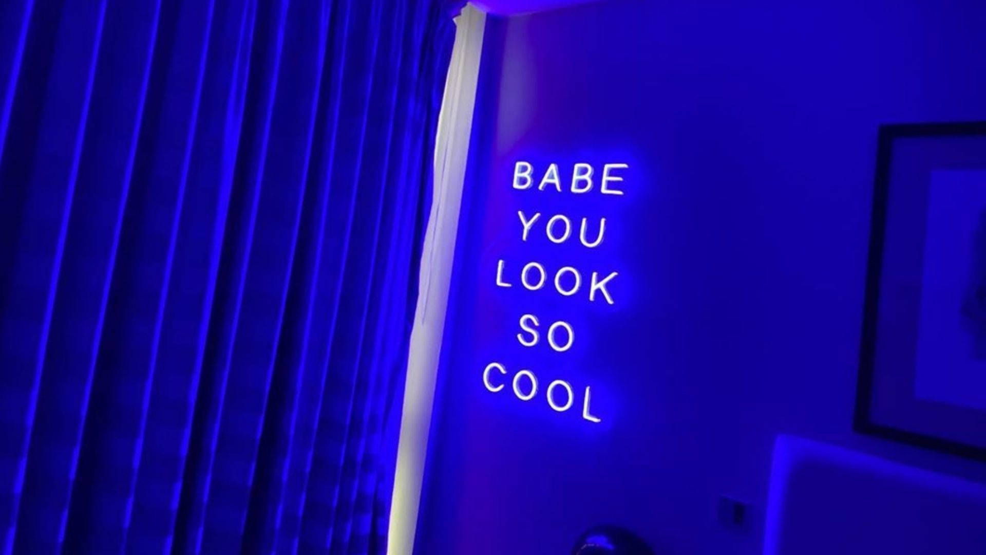 Neon blue sign with the words 'Babe You Look So Cool' mounted on a wall, adding a vibrant and stylish touch to a room bathed in blue light
