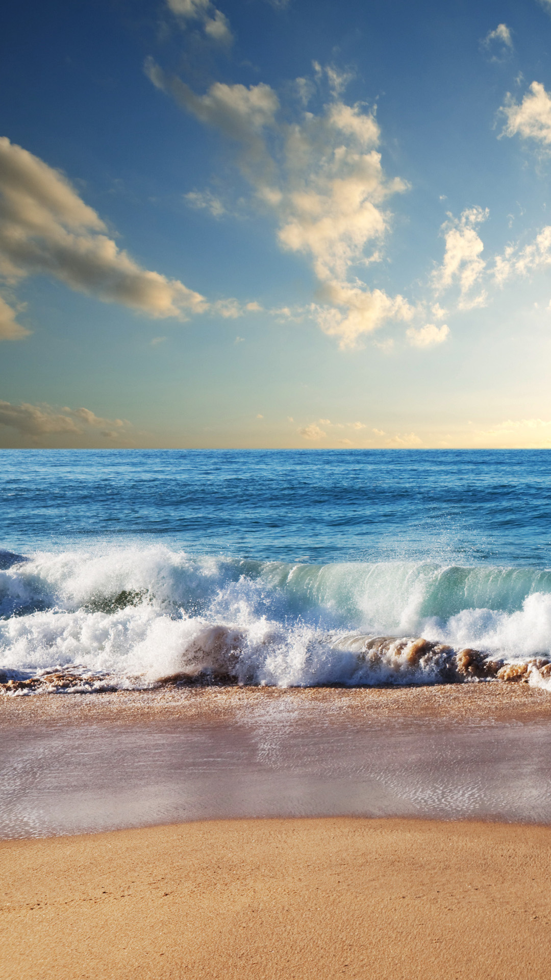 Ocean waves crashing on a sandy beach under a blue sky with white clouds