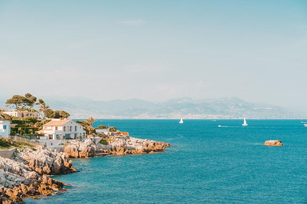 A tranquil blue ocean scene with a few boats and houses on the Antibes coast offering a serene and picturesque backdrop