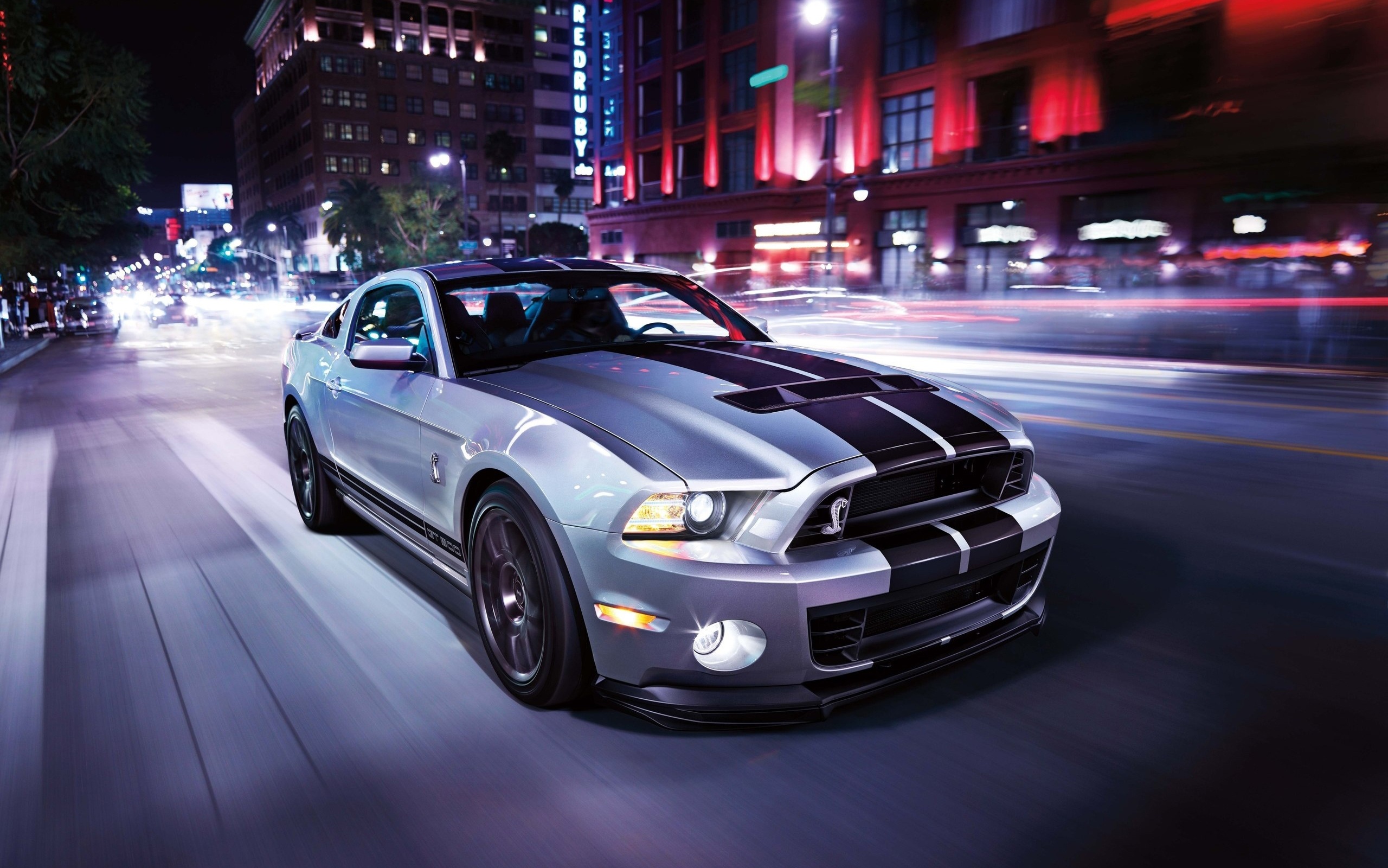 A silver Ford Mustang Shelby GT500 speeding down a city street at night