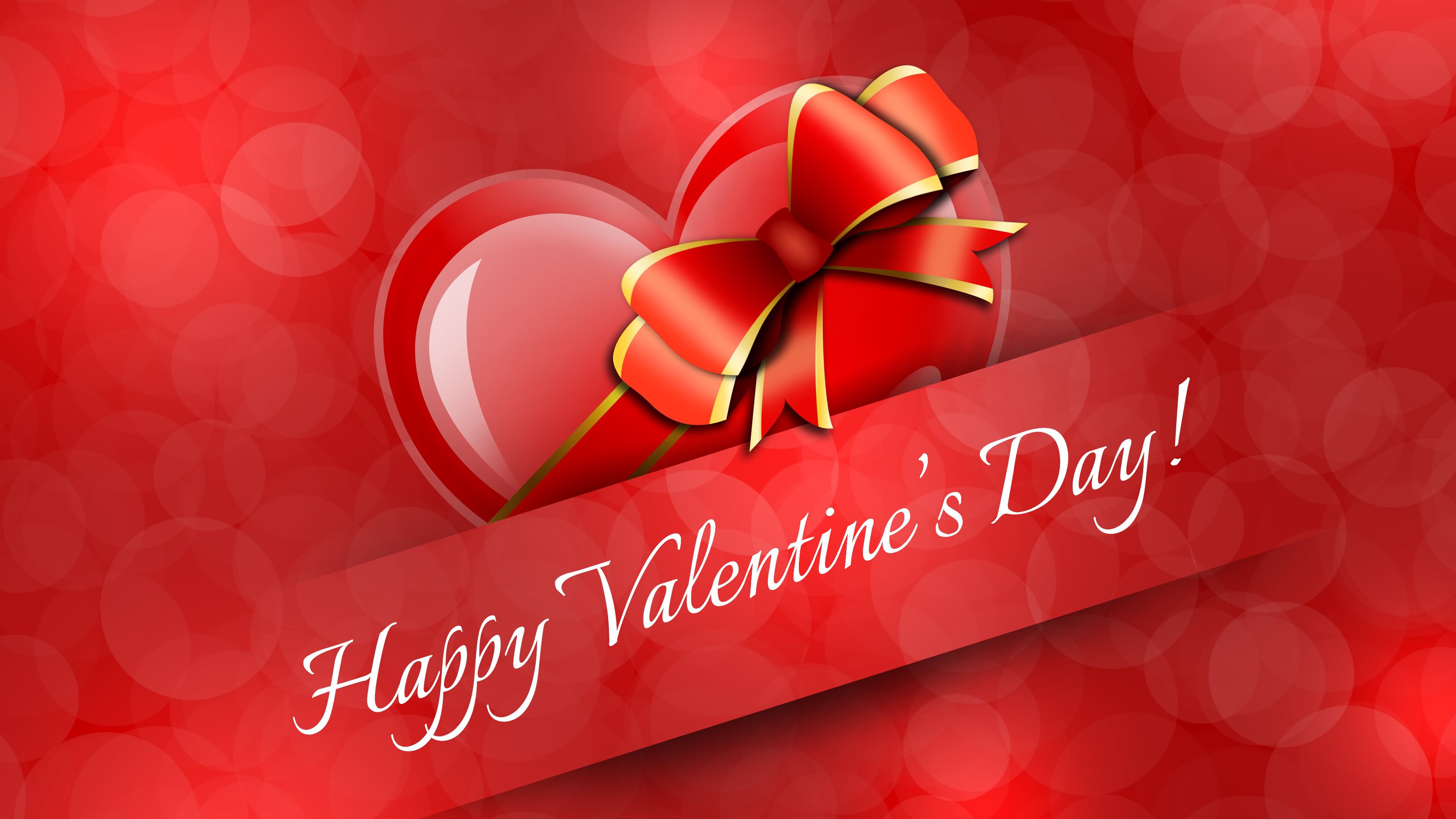 A Valentine's Day greeting image featuring a red heart with a shiny red ribbon and gold trim against a blurred bokeh red background