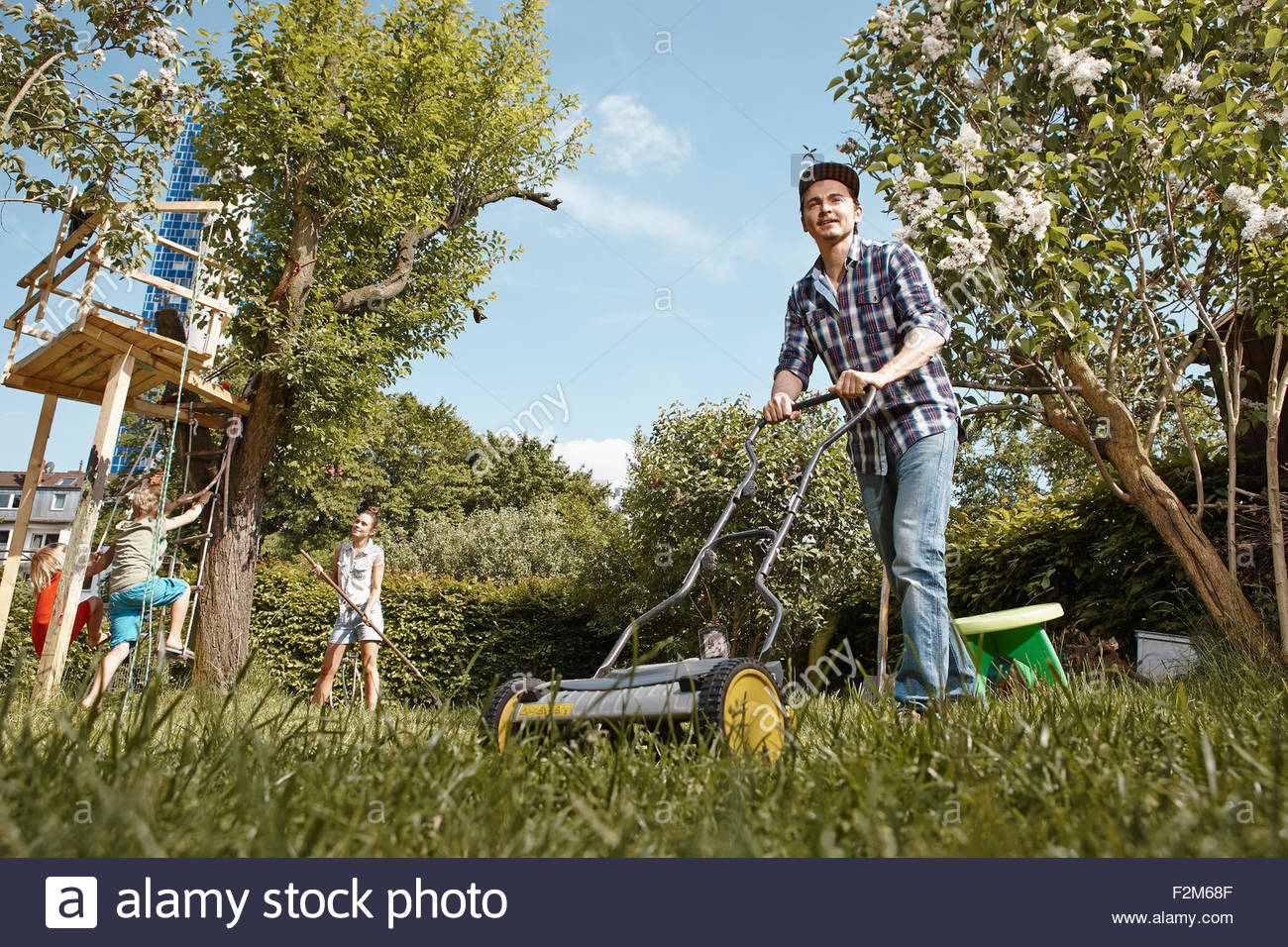Man Mowing Lawn In Garden With Family Background Stock Photo