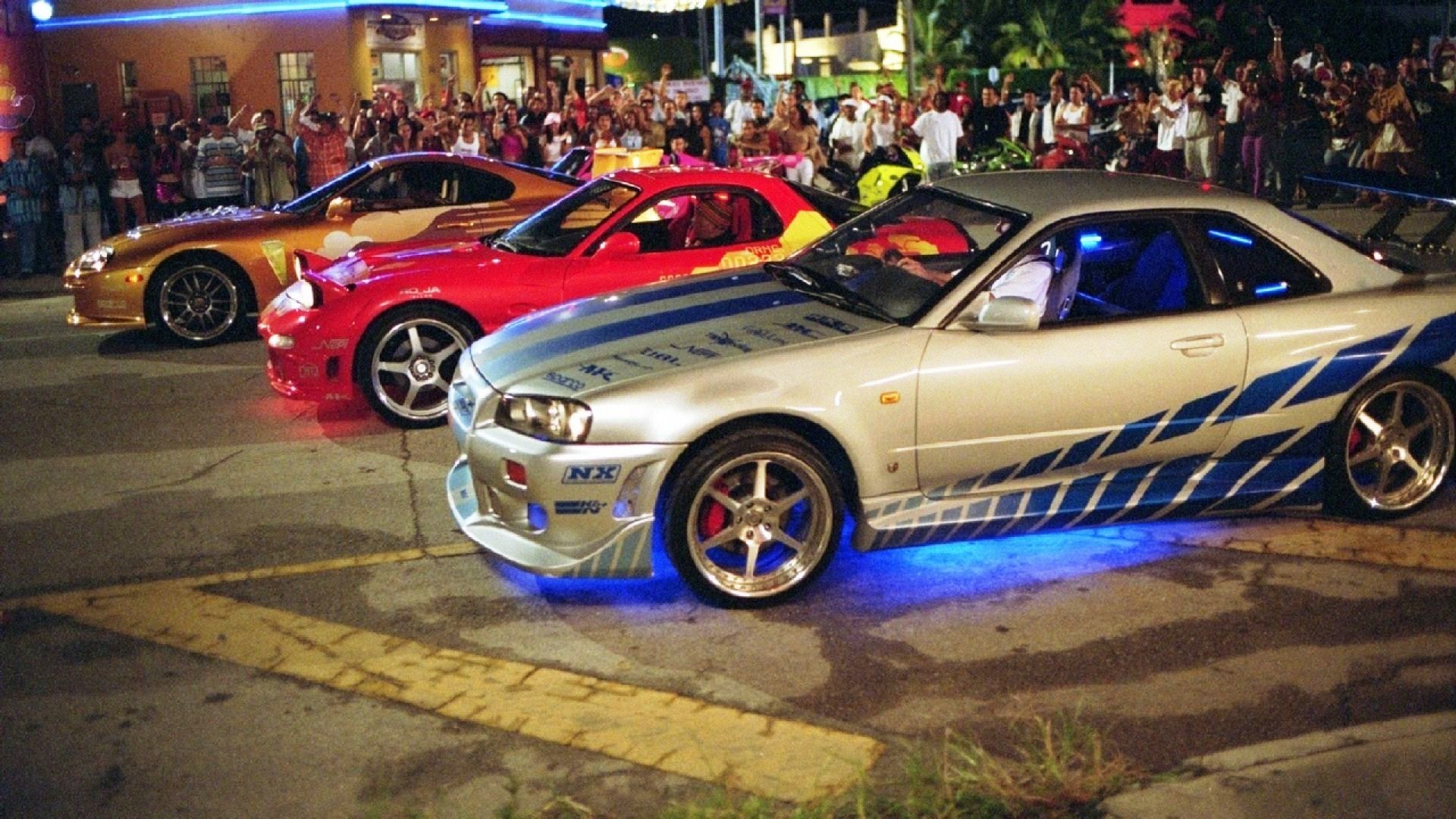 Three modified sports cars from the Fast and Furious movie franchise lined up for a street race at night
