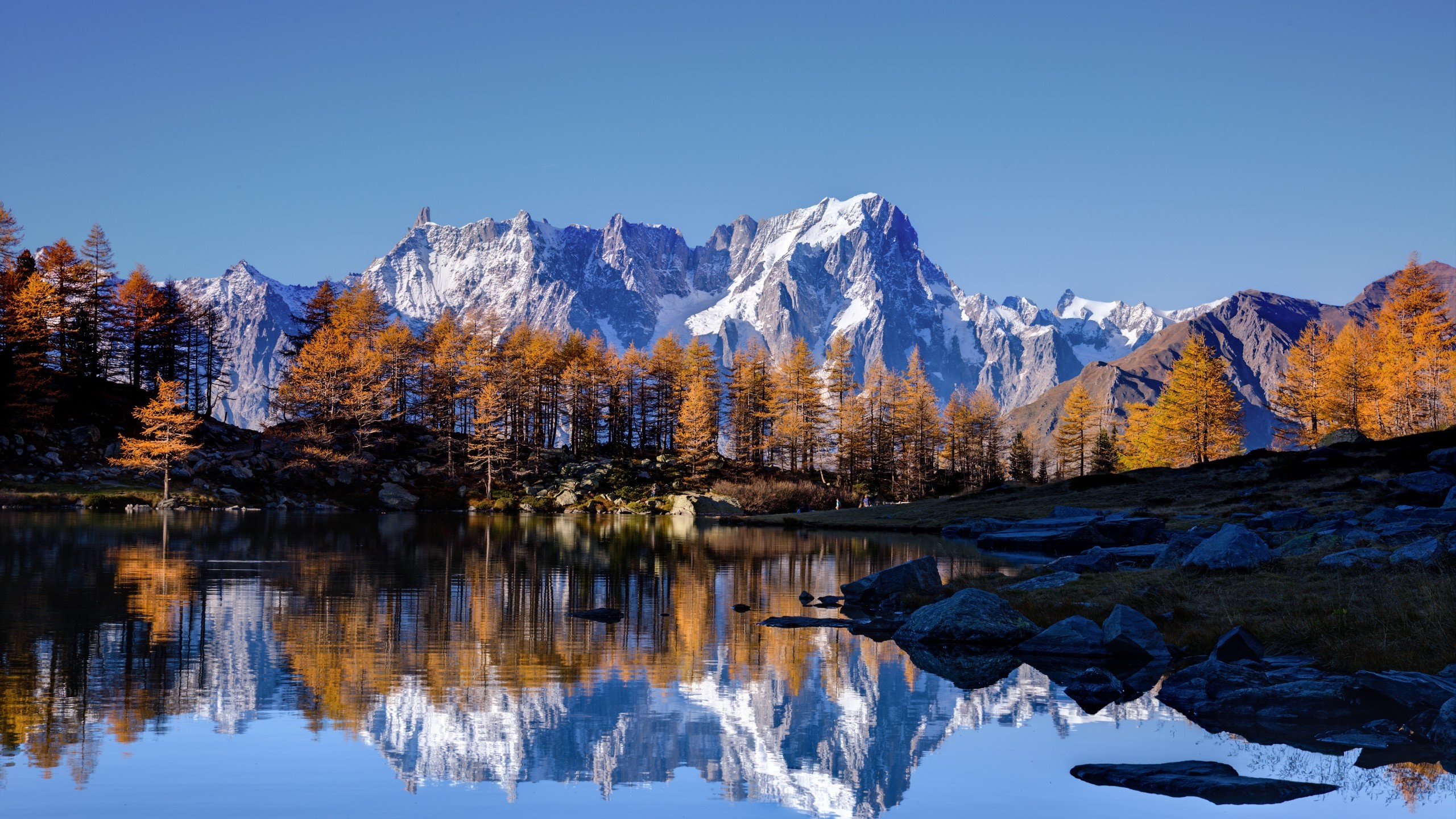 Stunning 5K HD wallpaper of a pristine alpine lake reflecting snow-capped mountains and golden autumn trees
