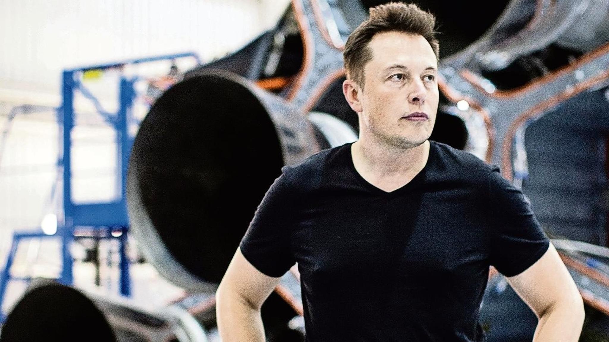 Elon Musk, CEO of SpaceX and Tesla, stands confidently in front of a spacecraft component in a manufacturing facility
