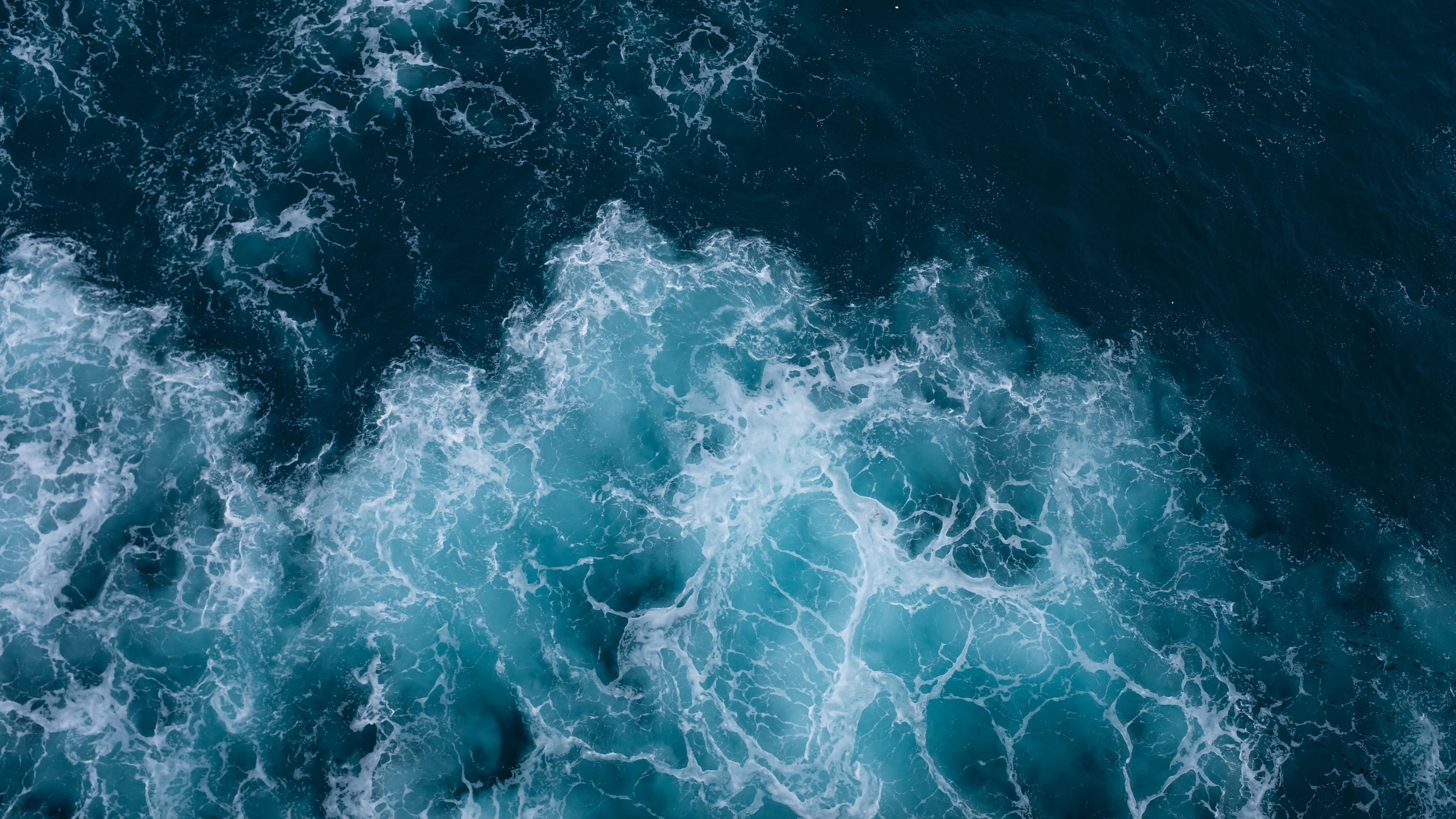 A top-down view of dark blue ocean water with turquoise foamy waves
