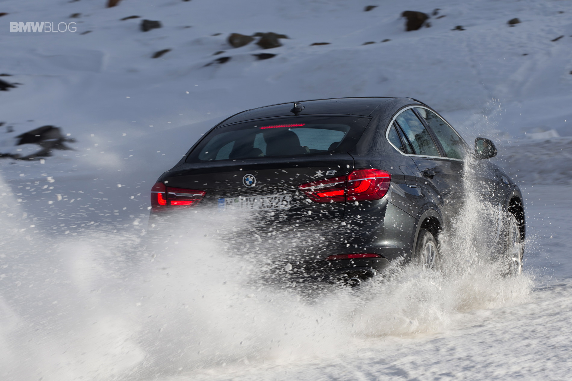 BMW X6 speeding through snowy terrain, kicking up a flurry of snow and ice particles