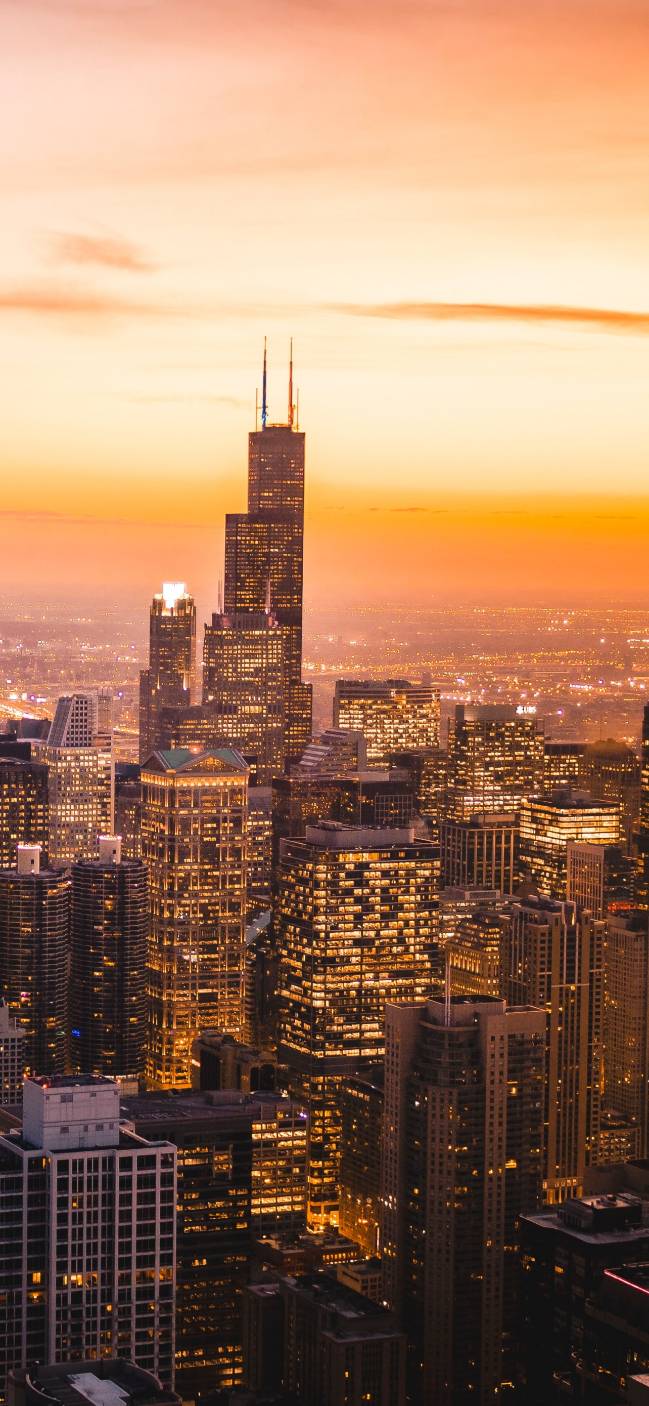 A stunning sunset over the Chicago skyline, with the Willis Tower prominently featured among the illuminated buildings
