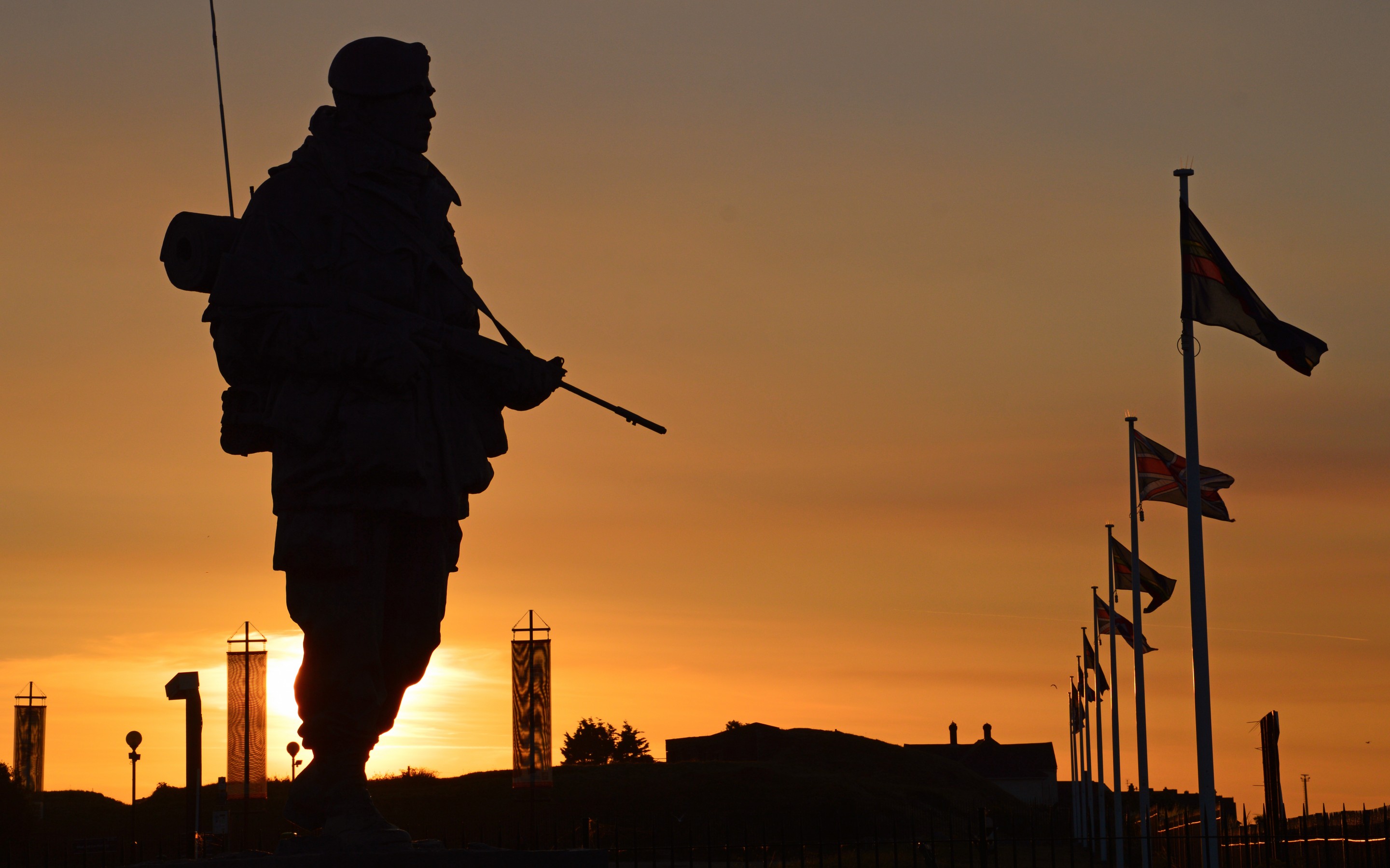 Silhouette of a Commando Memorial Statue against a vibrant sunset backdrop with flags waving in the background