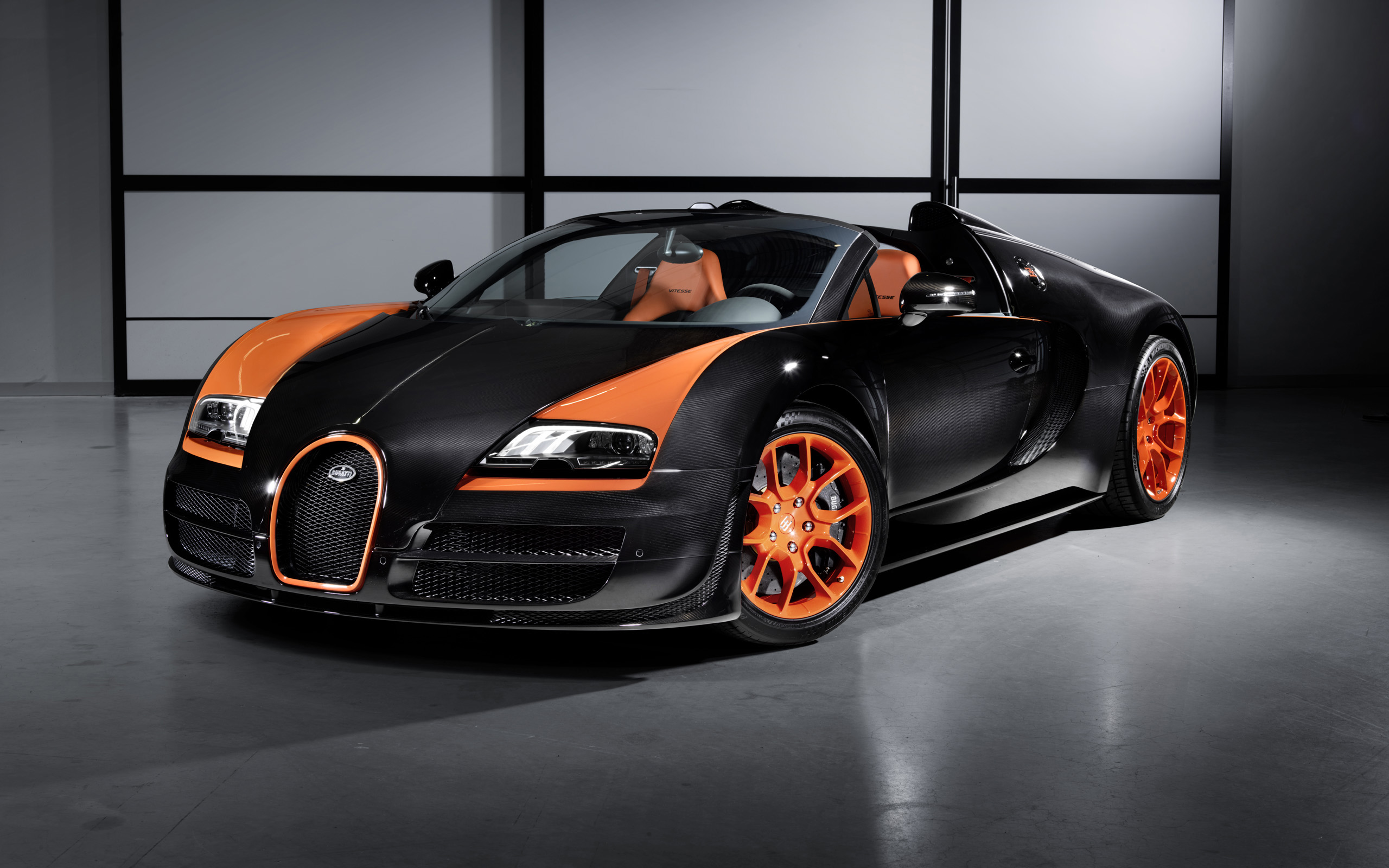 A black and orange Bugatti Veyron Grand Sport, parked in a showroom, with visible carbon fiber bodywork and orange accents on the wheels and body
