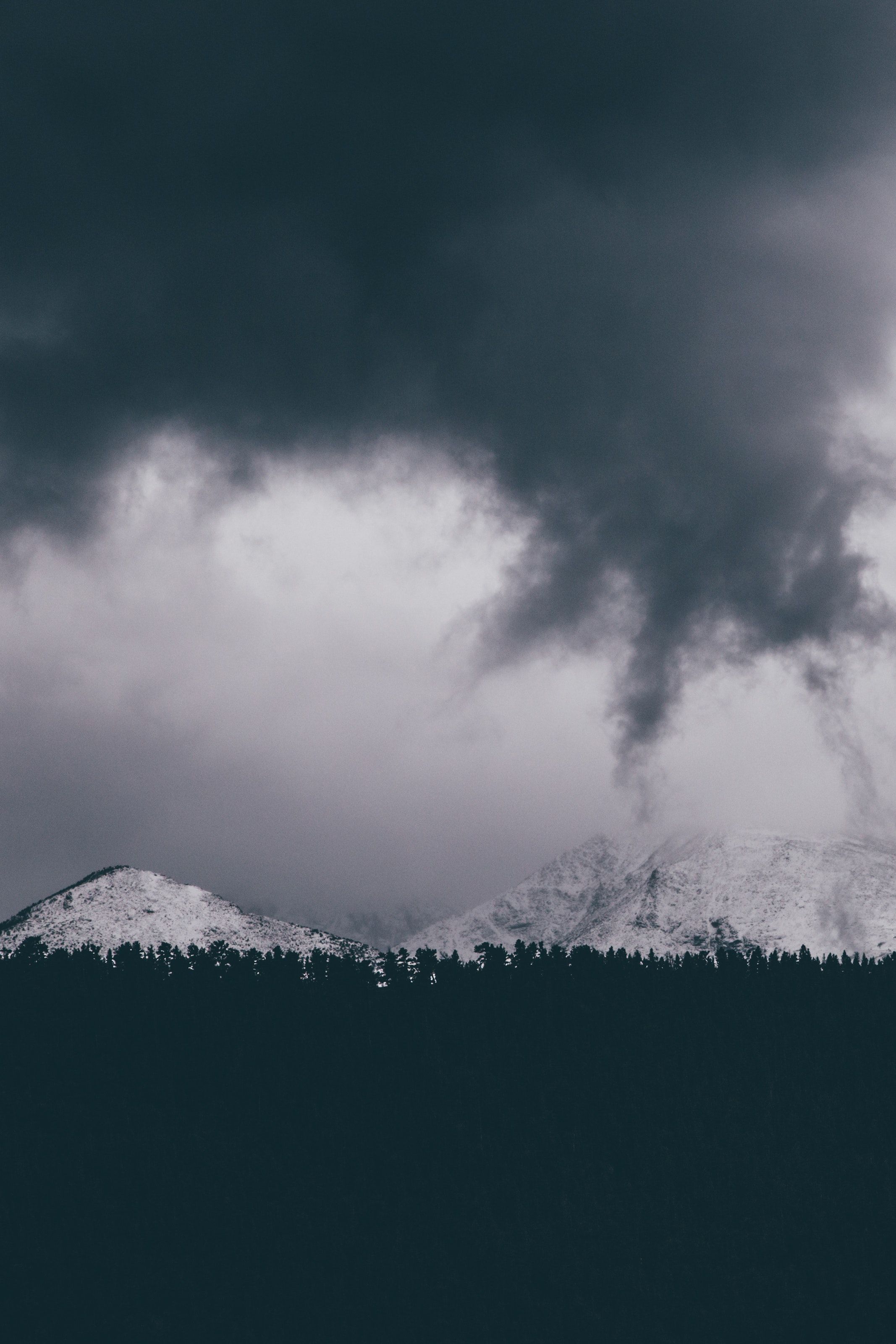 A Bleak Shot Of White Mountains Over Dark Treeline On Cloudy