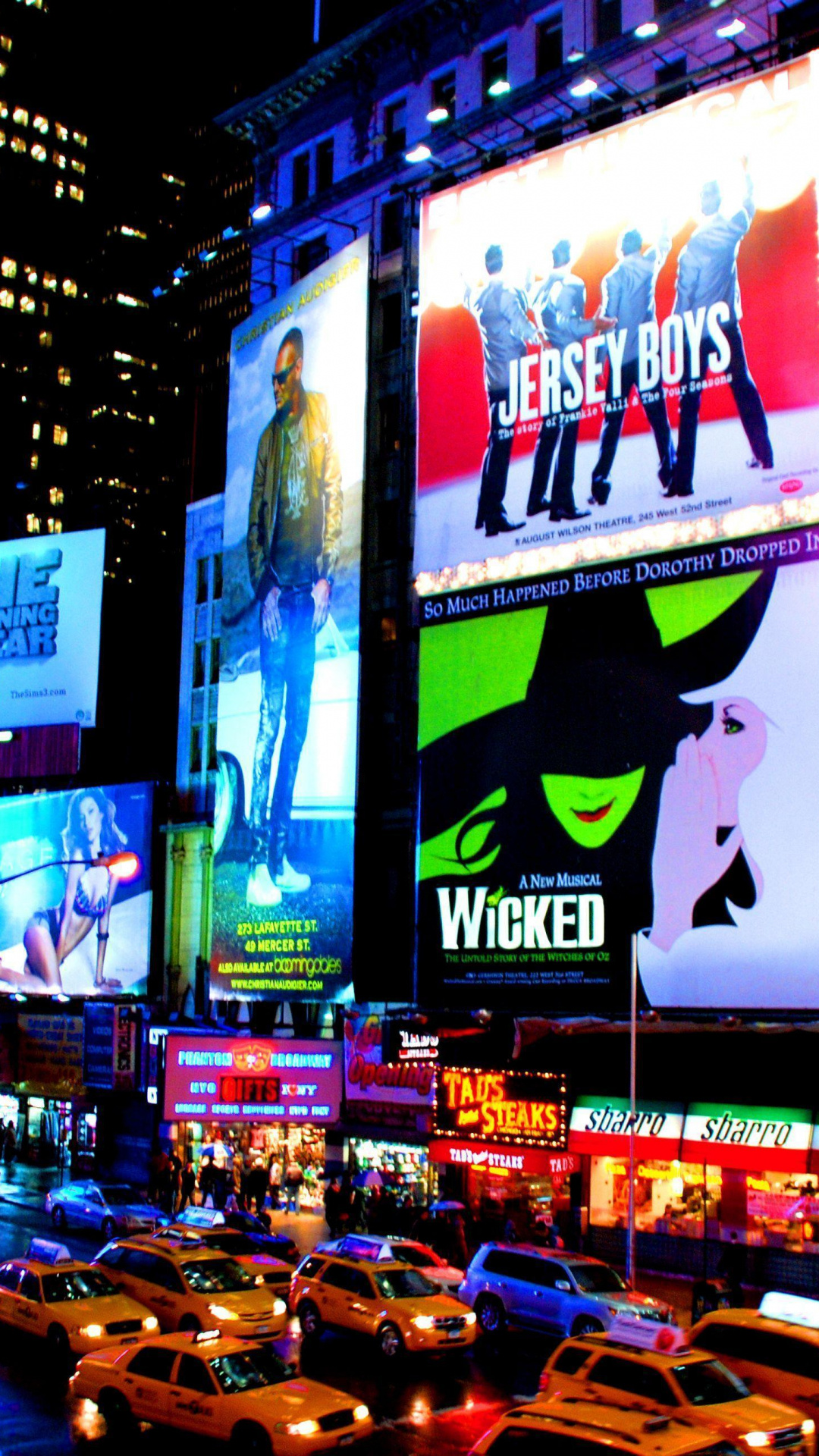 A vibrant night-time view of Times Square in New York City, showcasing illuminated billboards for Broadway shows like Jersey Boys and Wicked, amidst the bustling city traffic