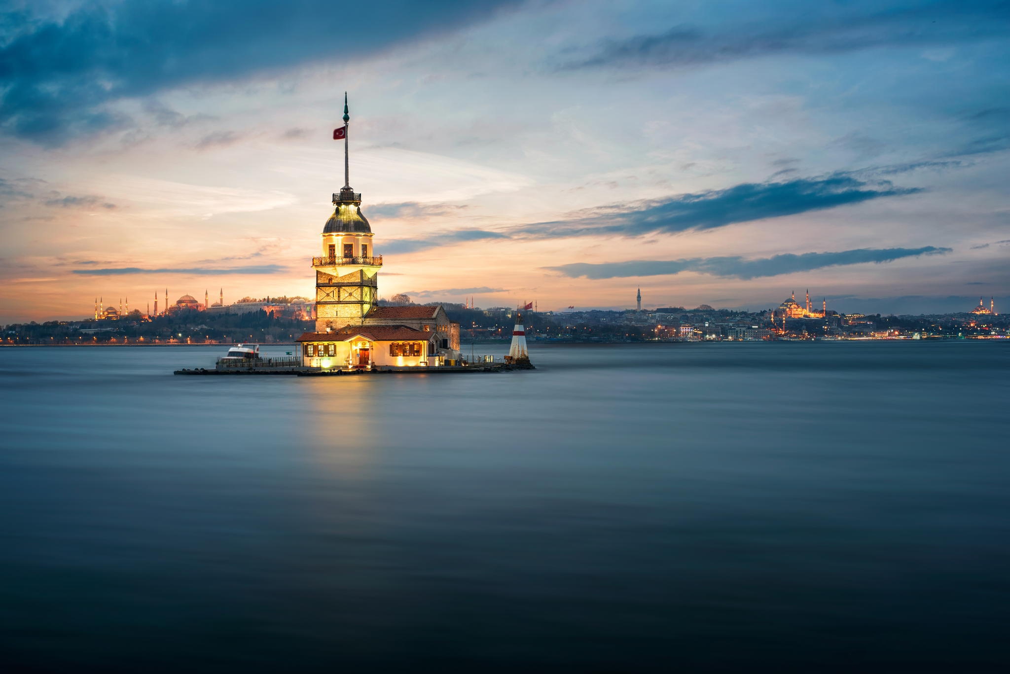 The Maiden's Tower, lit up at night, stands in the Bosphorus Strait with the Istanbul skyline in the background