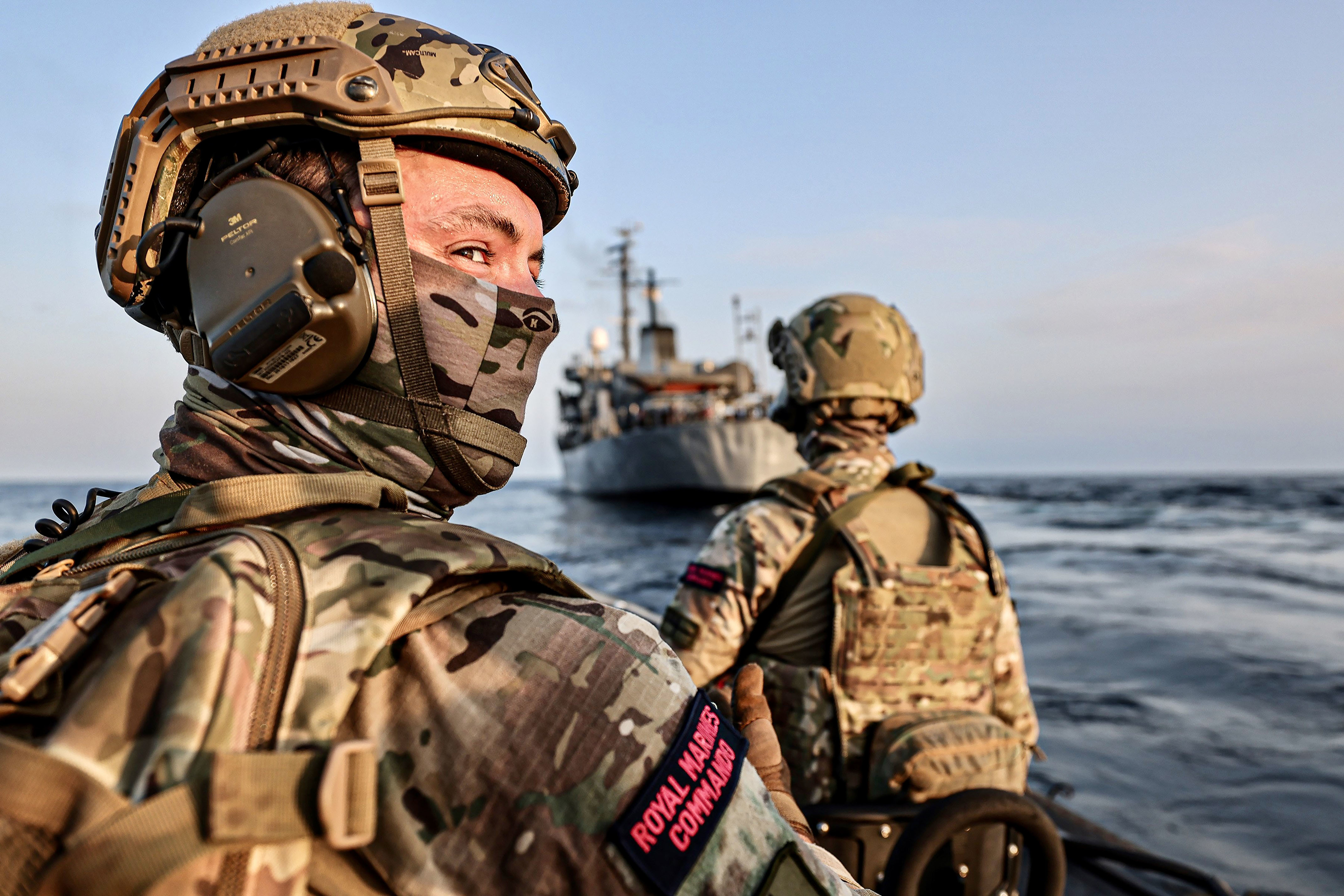 Two Royal Marines Commandos on a boat with a naval ship in the background
