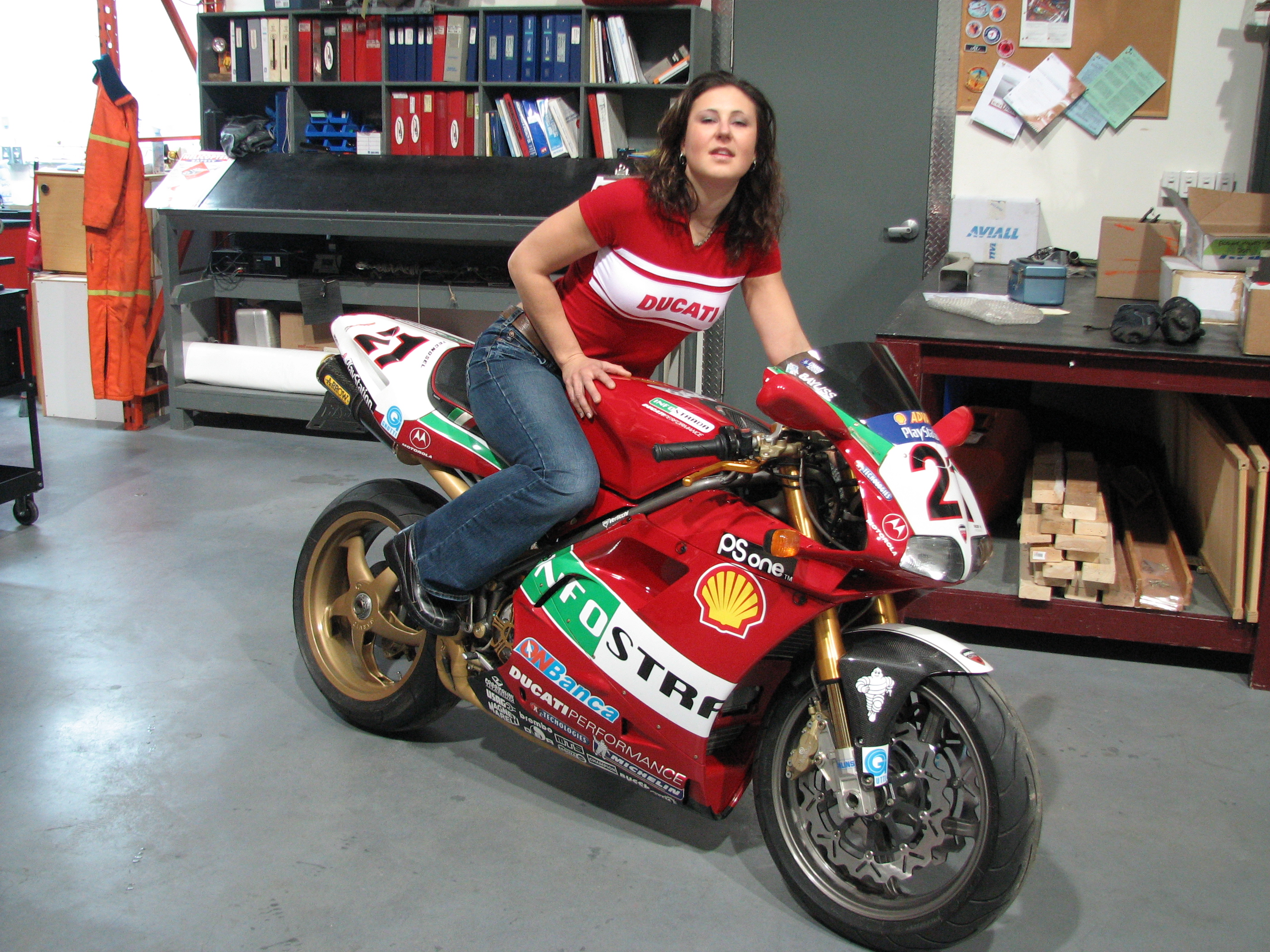 A woman posing with a Ducati 996 racing motorcycle in a garage setting