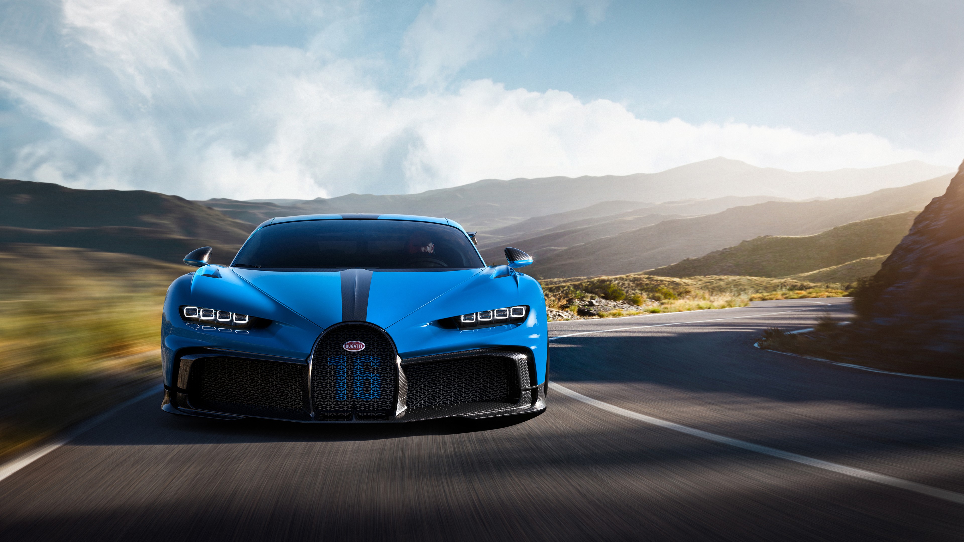 A blue Bugatti Chiron Super Sport speeds along a winding mountain road, showcasing its sleek design and powerful performance