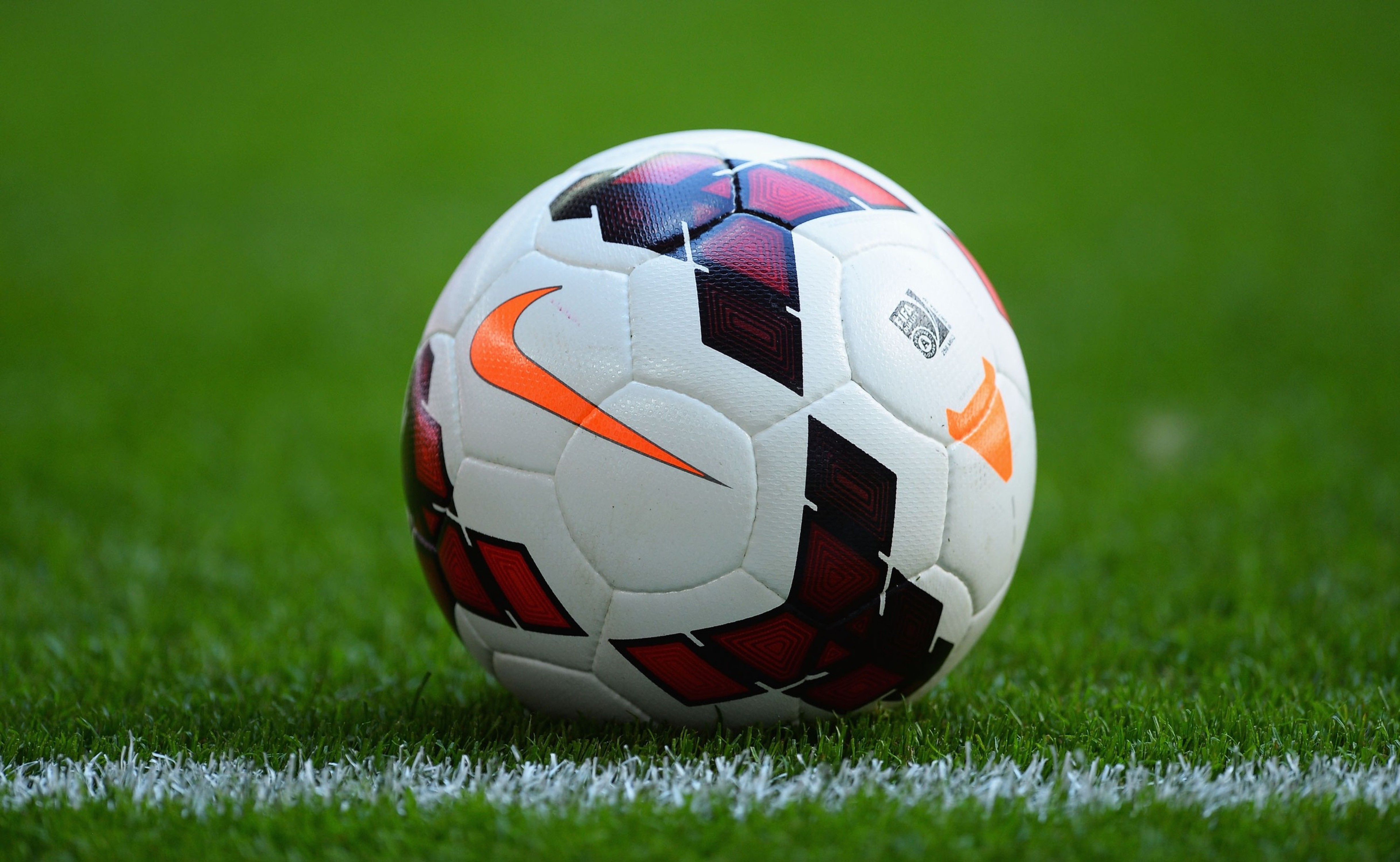 Close-up of a Nike soccer ball on a lush green field, resting near the white boundary line