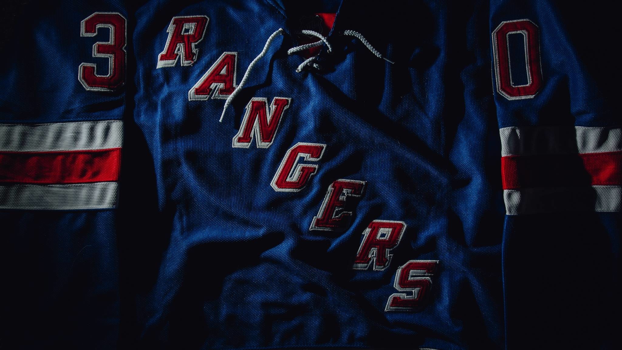 Close-up of a New York Rangers jersey, showcasing the team's iconic blue color, red and white stripes, and 'Rangers' lettering