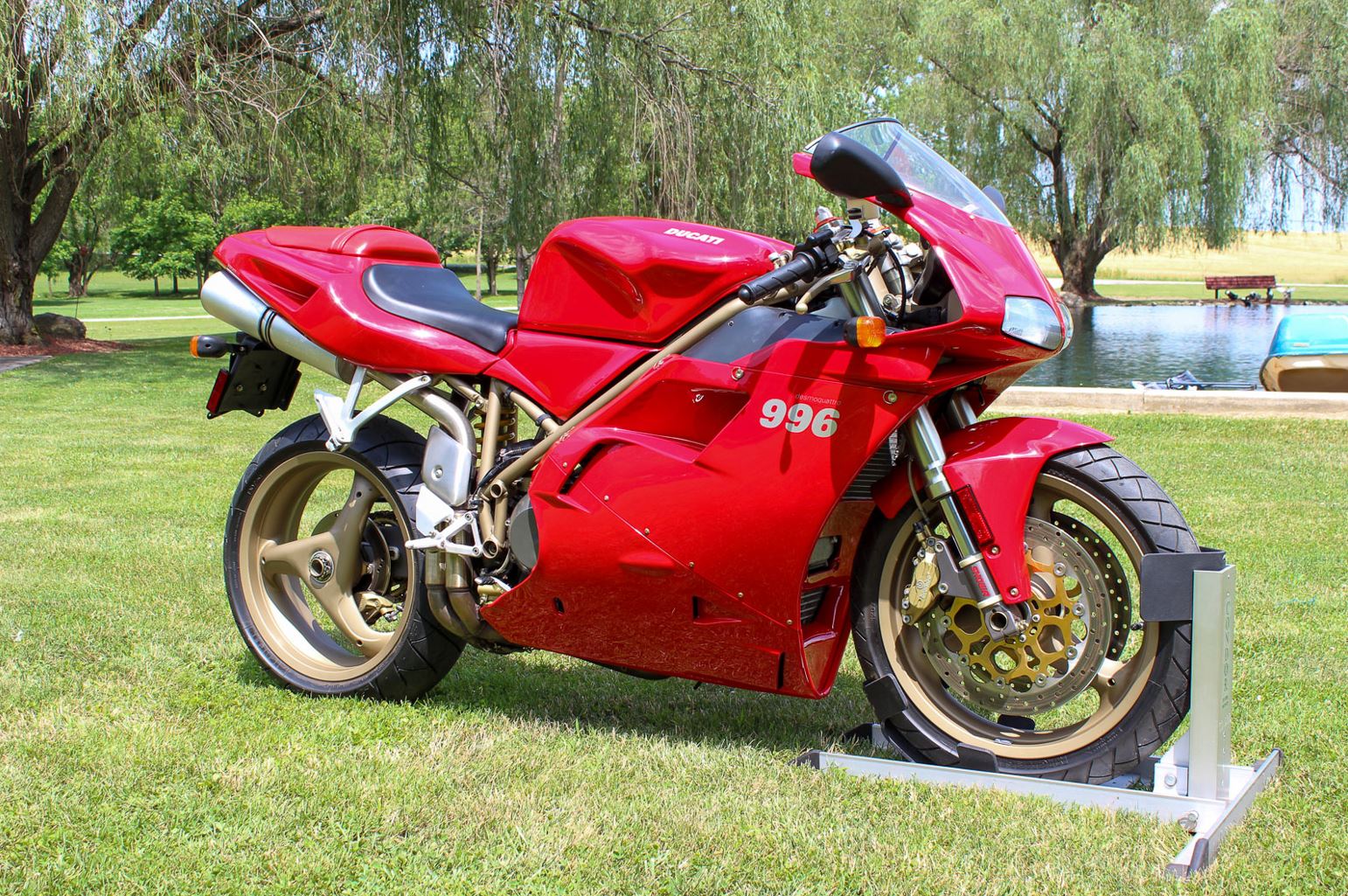 Red Ducati 996 sportbike parked on grass next to a pond