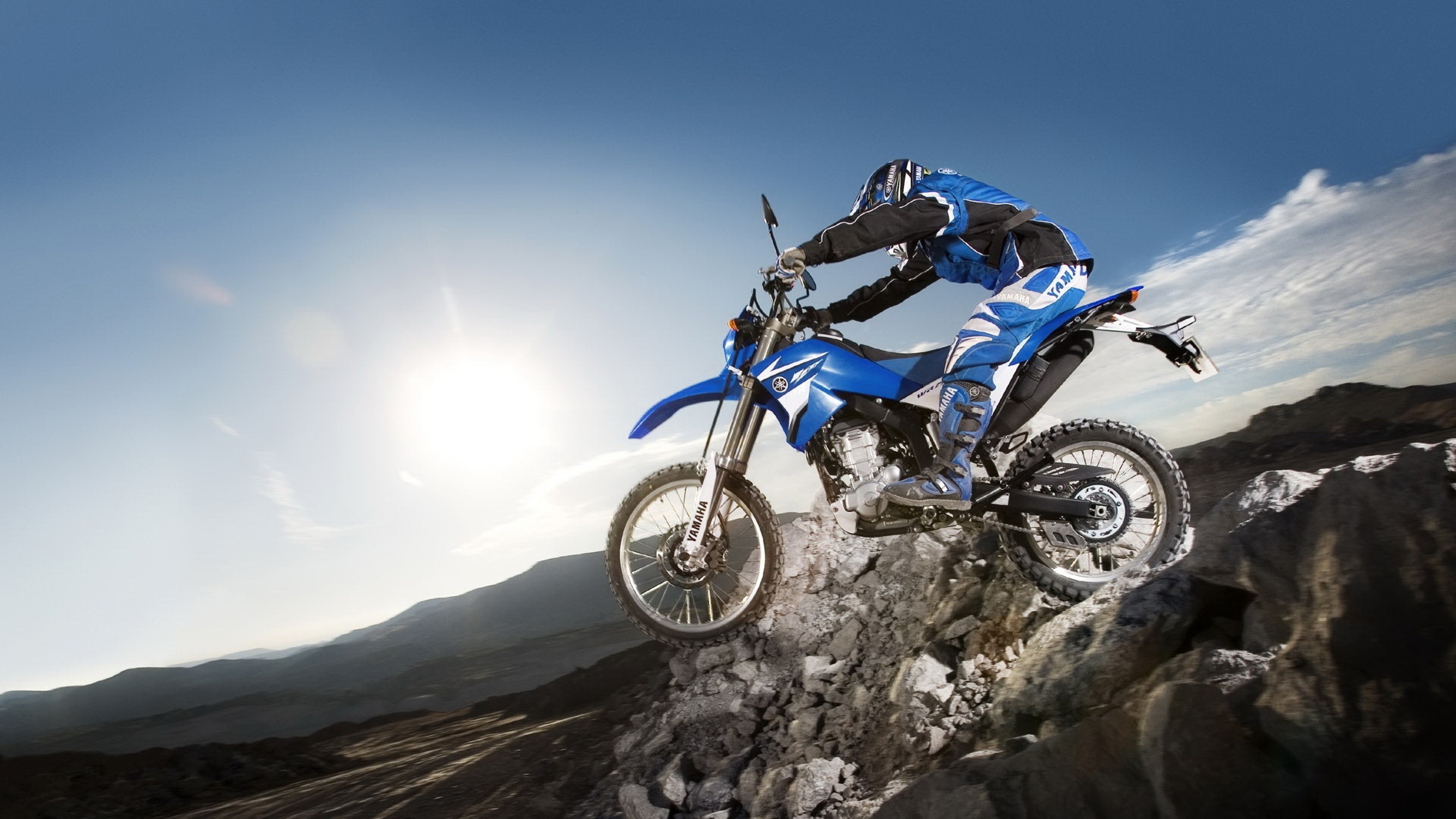A Yamaha dirt bike tackles a rocky incline against a bright blue sky, showcasing off-road adventure