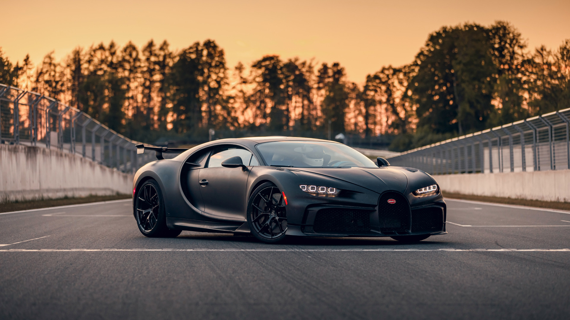 A sleek, black Bugatti Chiron Super Sport on a race track at sunset