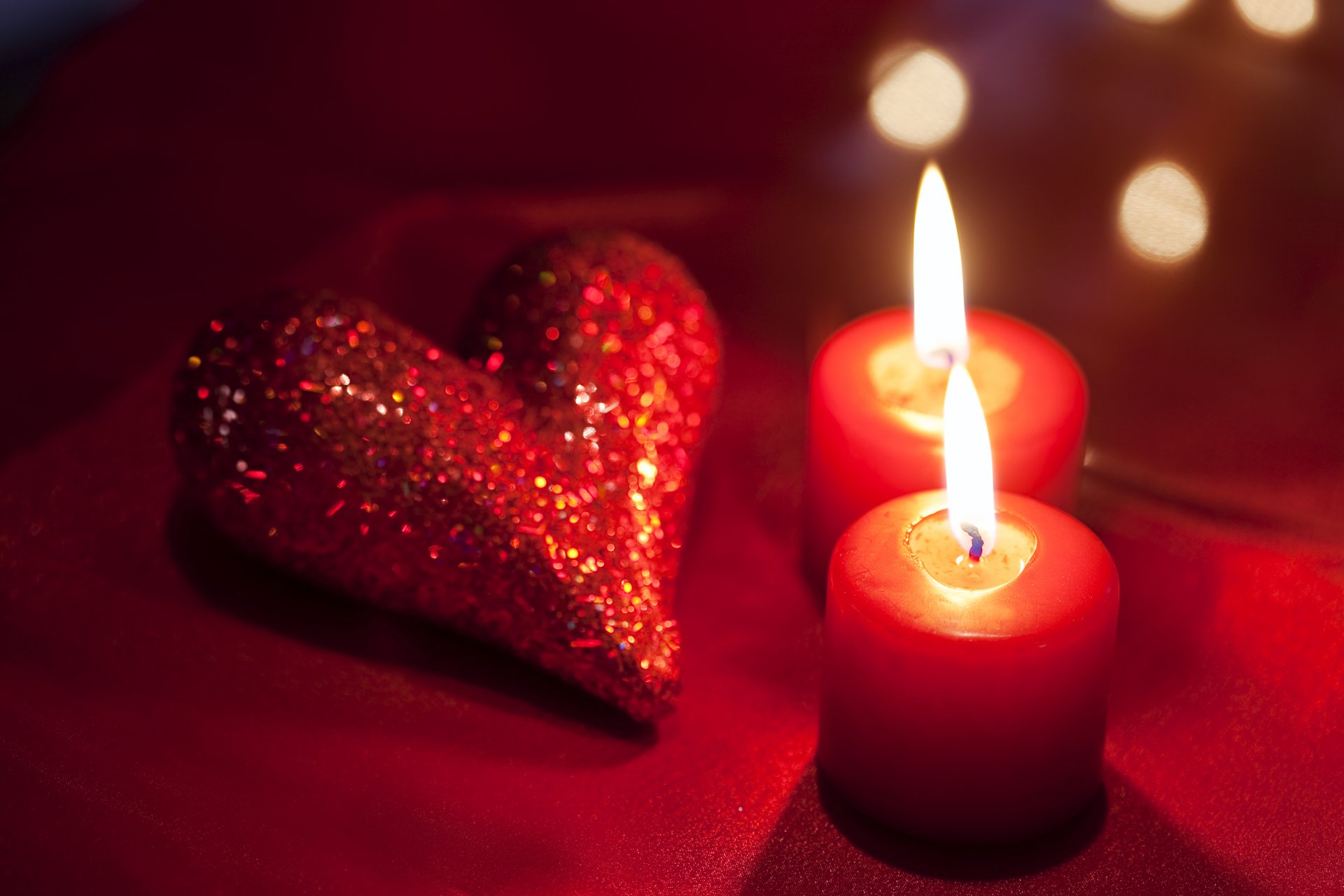 Two lit red candles and a red glitter heart on a red tablecloth, creating a romantic Valentine's Day atmosphere