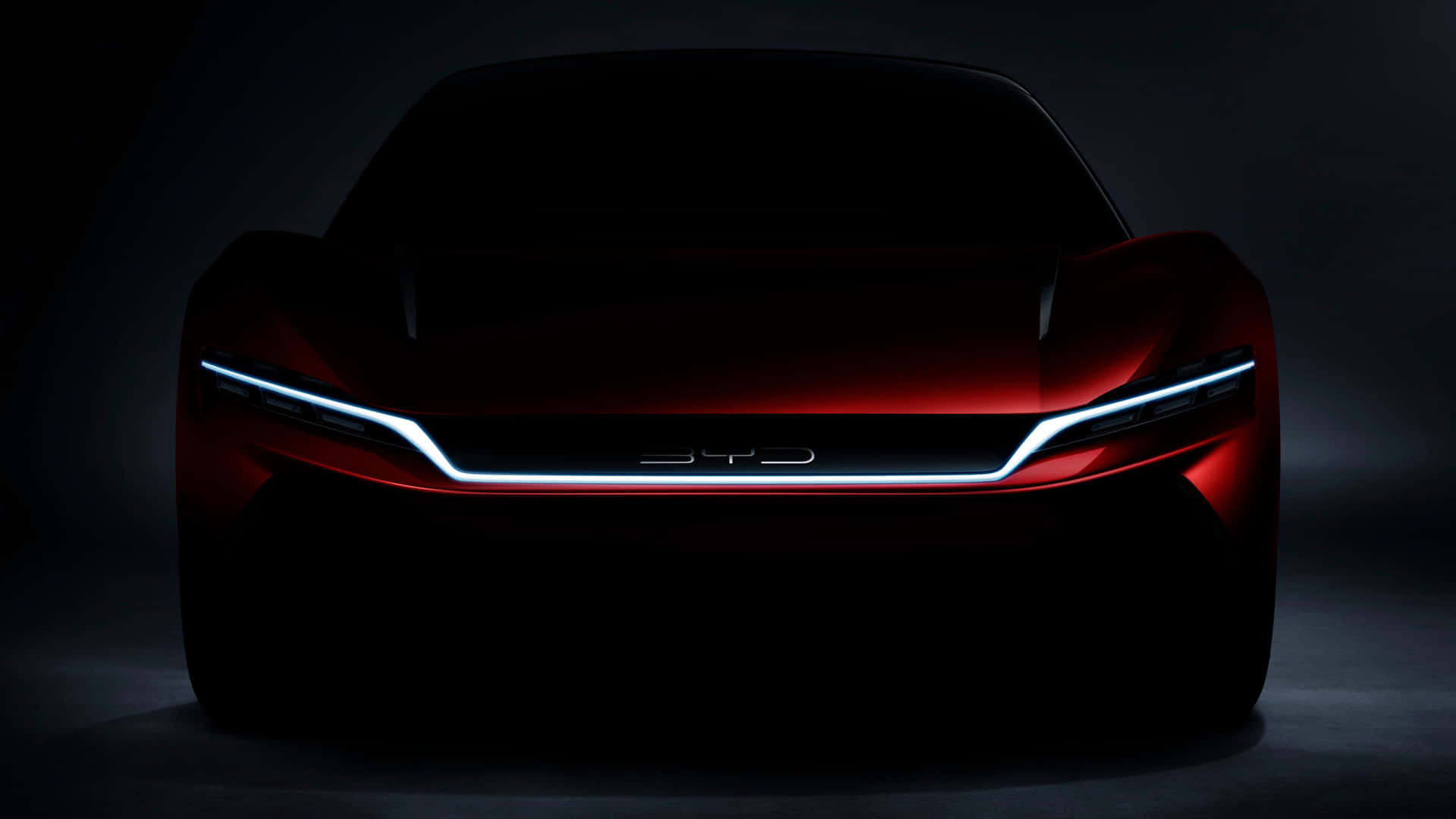 A shadowy front view of the BYD Shark, a futuristic concept car, highlighting its sleek silhouette and illuminated logo