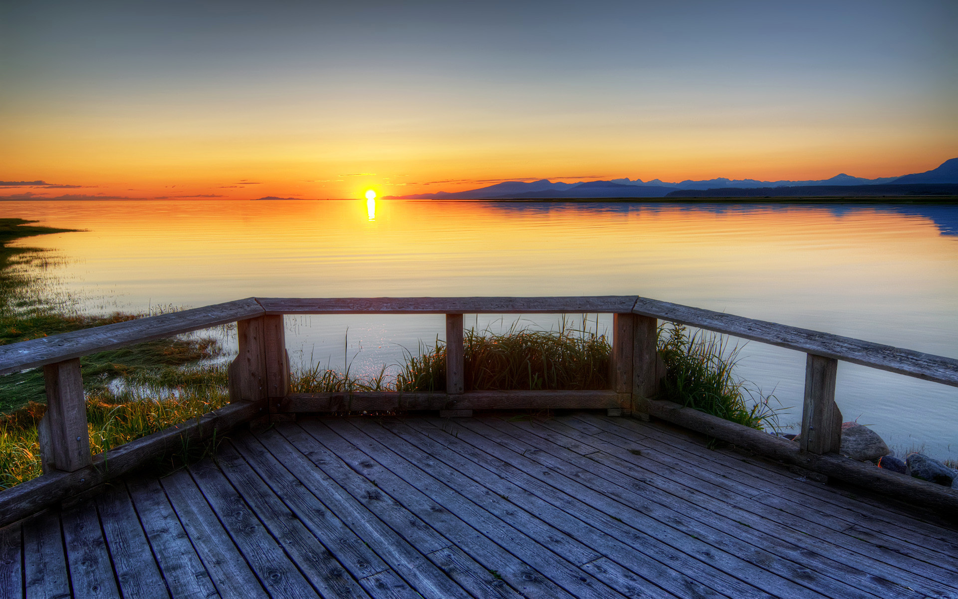 A serene sunset over a tranquil lake, viewed from a wooden deck