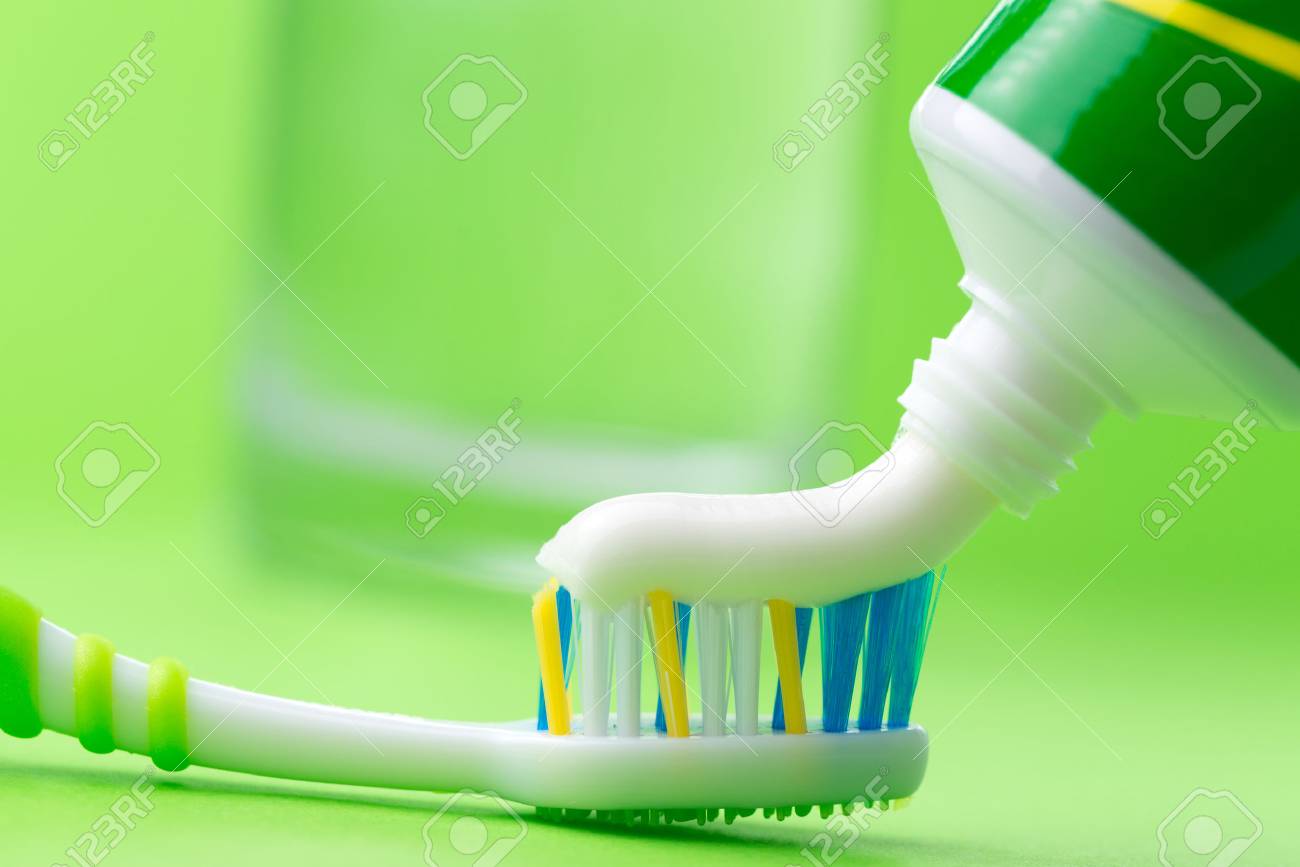 Close Up Of Squeezing Toothpaste On Toothbrush Green Background