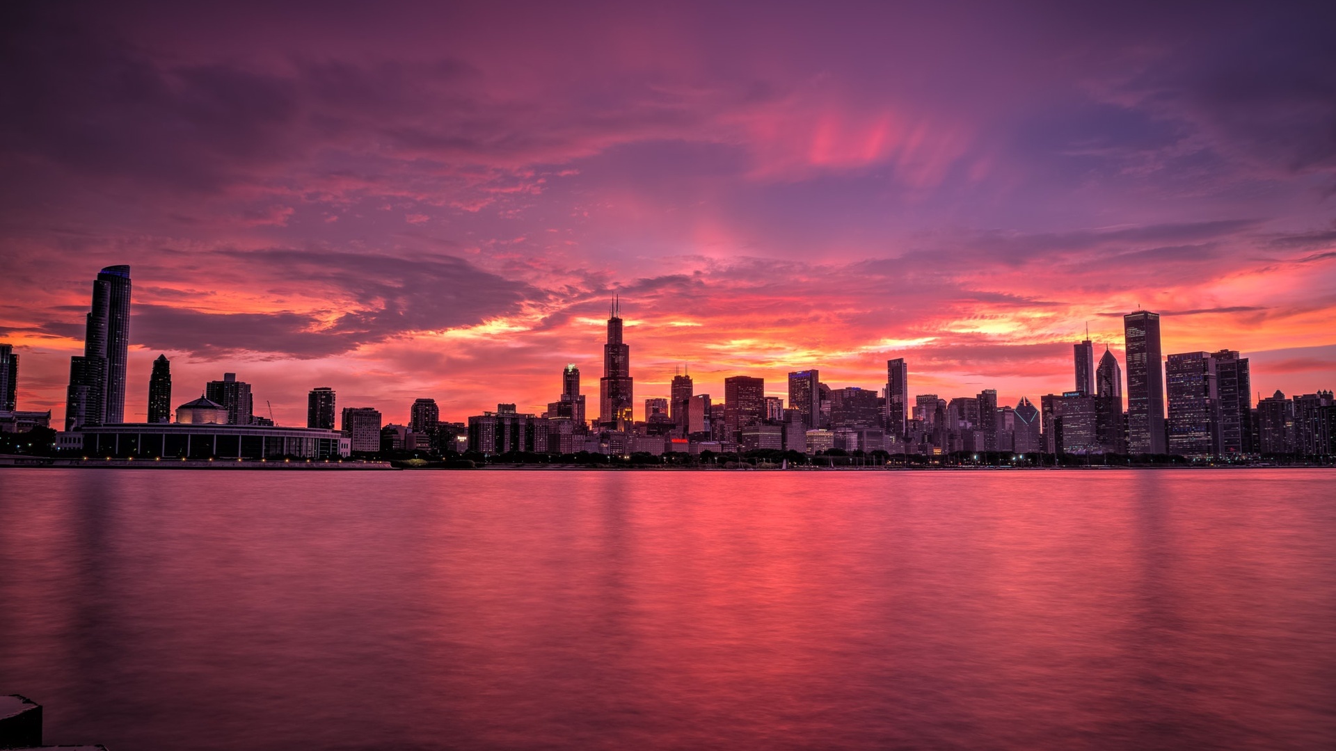 A breathtaking Chicago skyline at sunset, with vibrant pink and orange hues reflected in the calm waters of Lake Michigan