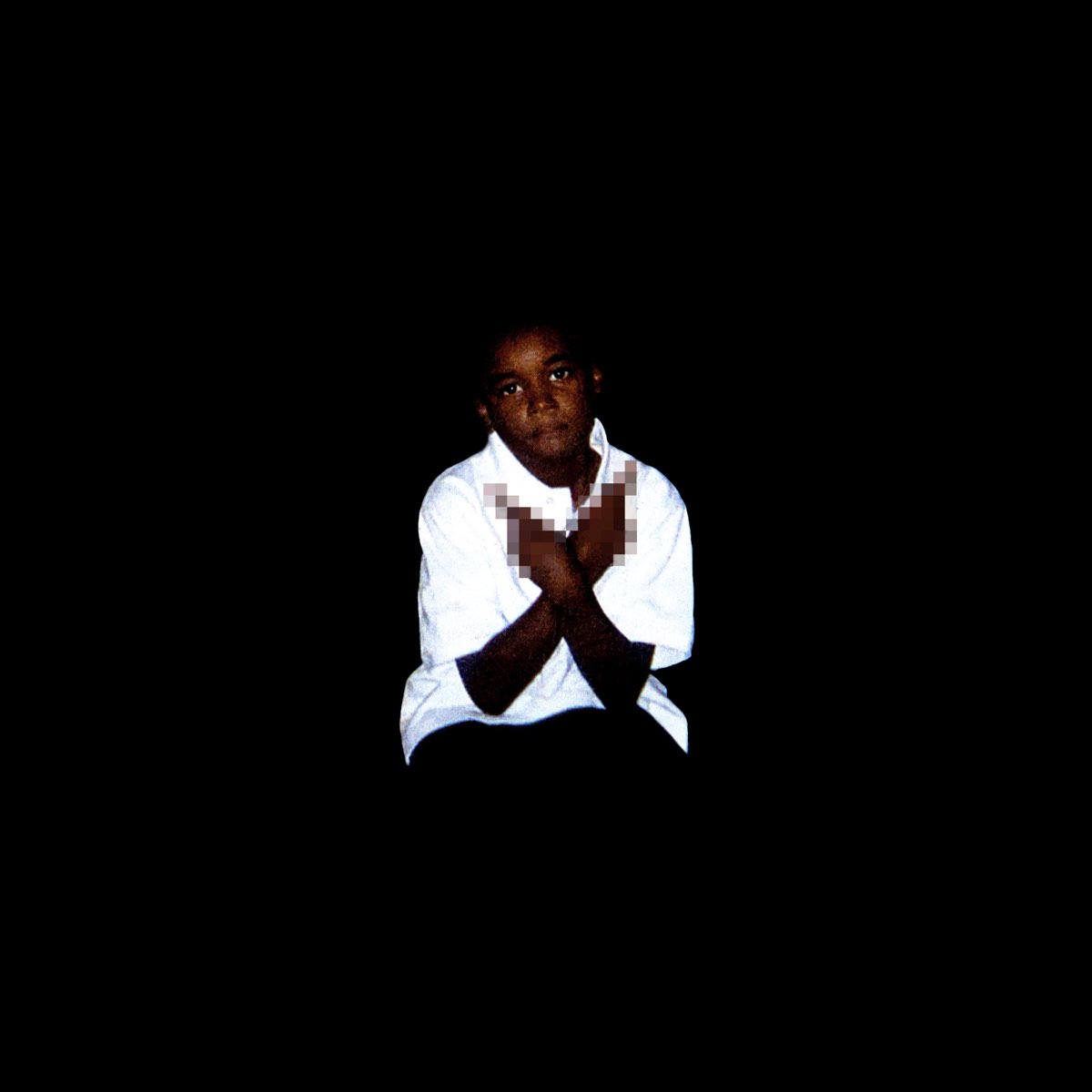 A young boy in a white shirt, against a dark background, with his arms crossed over his chest. The focus is on his serious expression, with his body fading into the shadows