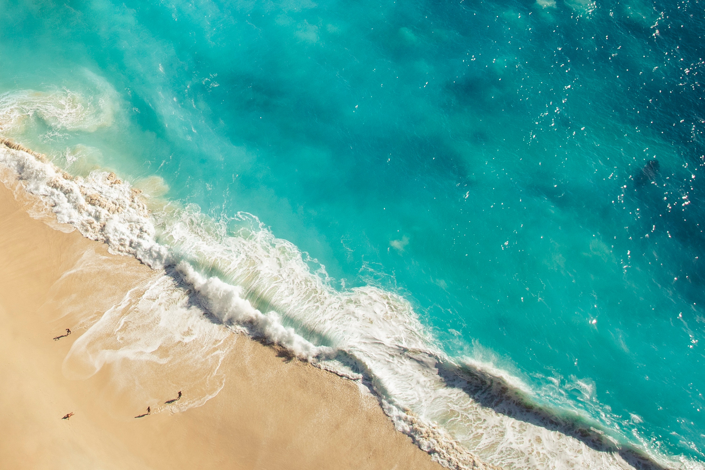 Aerial view of turquoise ocean waves crashing on a sandy beach