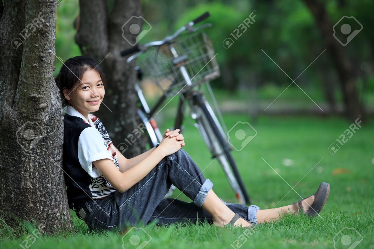 Woman Sitting In The Green Garden With Bicycle Background Stock