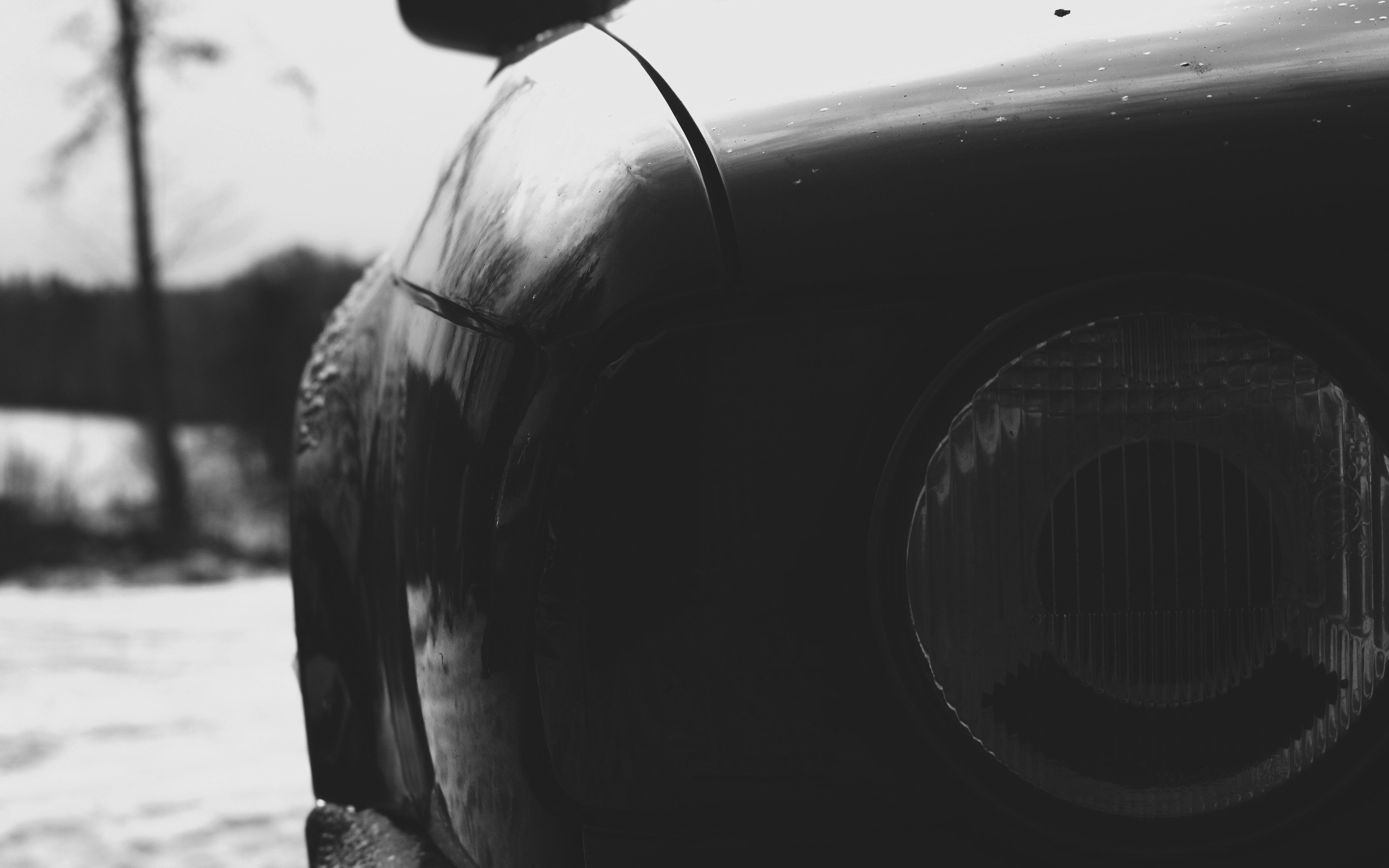 Black and white close-up of a BMW parked in the snow, focusing on the headlight and fender