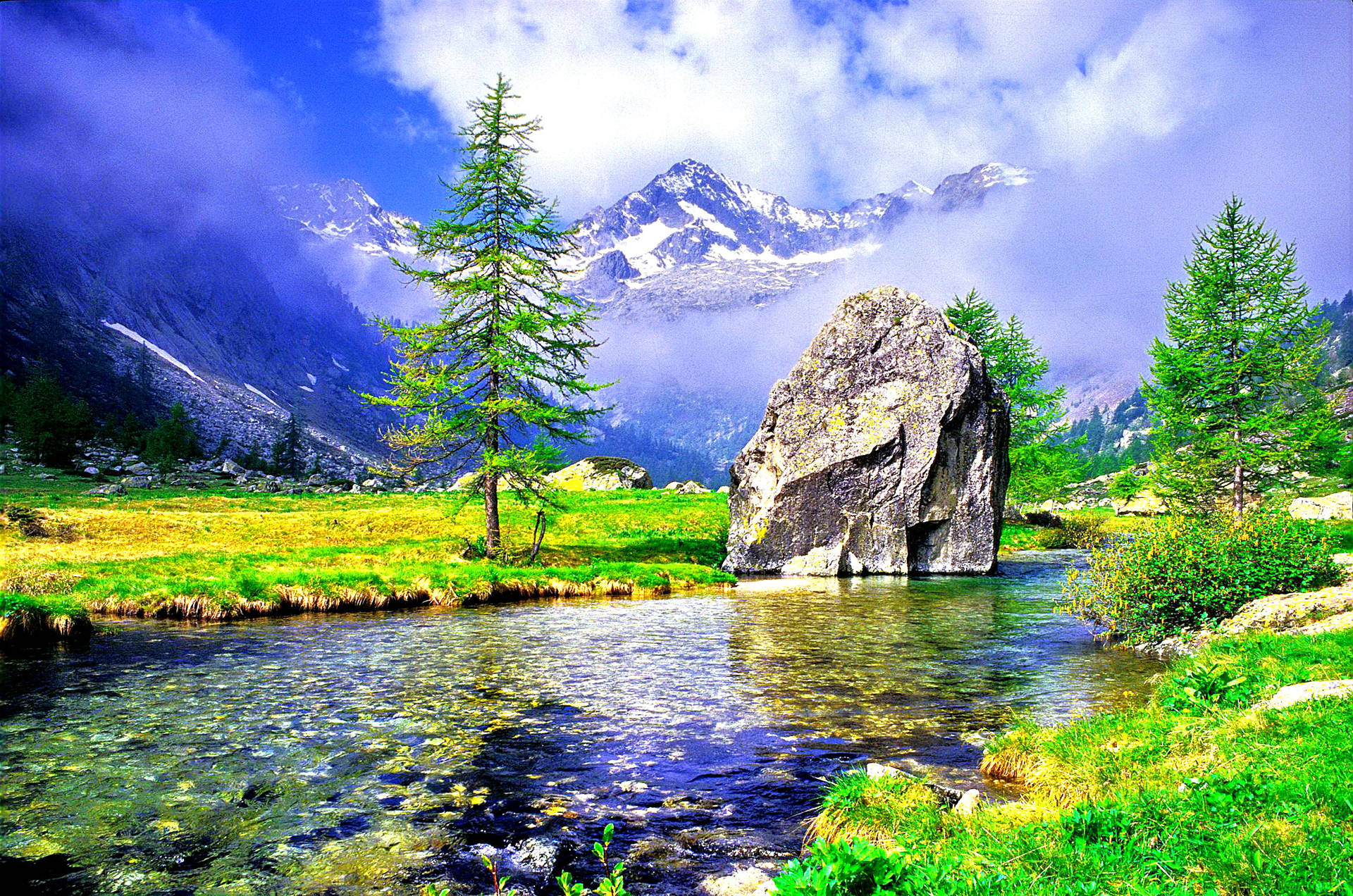 A breathtaking HD wallpaper showcasing a pristine alpine lake with crystal-clear water, surrounded by lush green meadows, towering evergreen trees, and majestic snow-capped mountains in the background