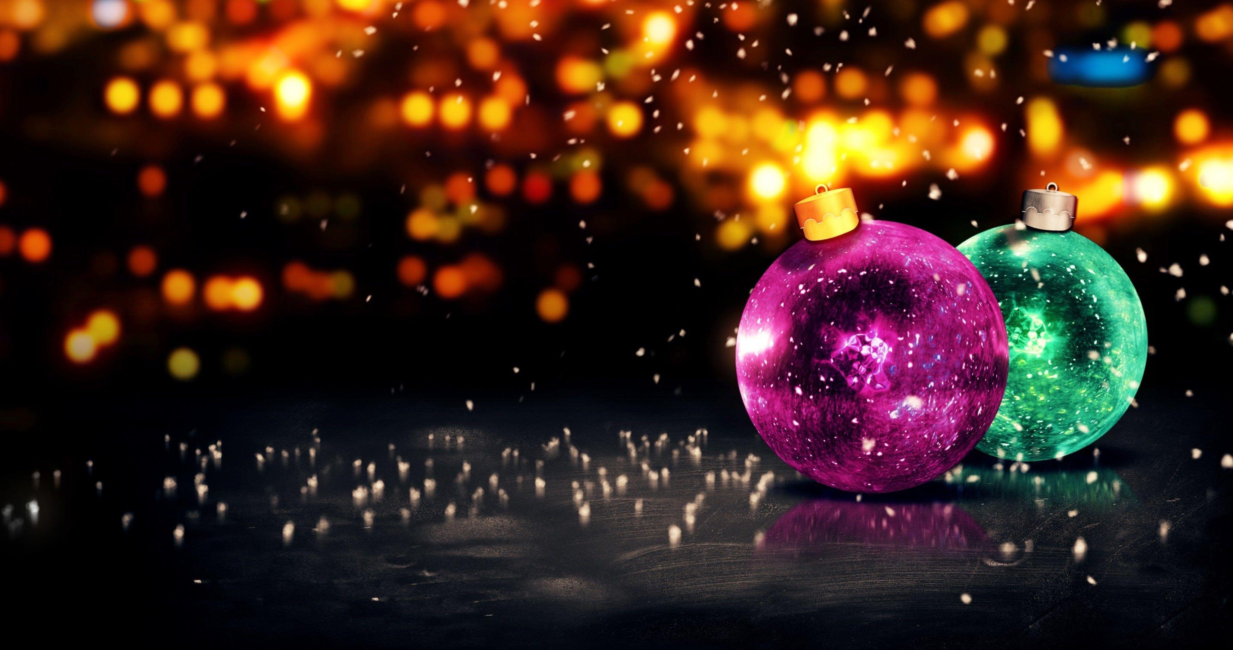 Two vibrant Christmas ornaments, one magenta and one teal, glow against a backdrop of blurred golden lights and falling snowflakes.  A dark, textured surface reflects the ornaments, adding to the festive atmosphere