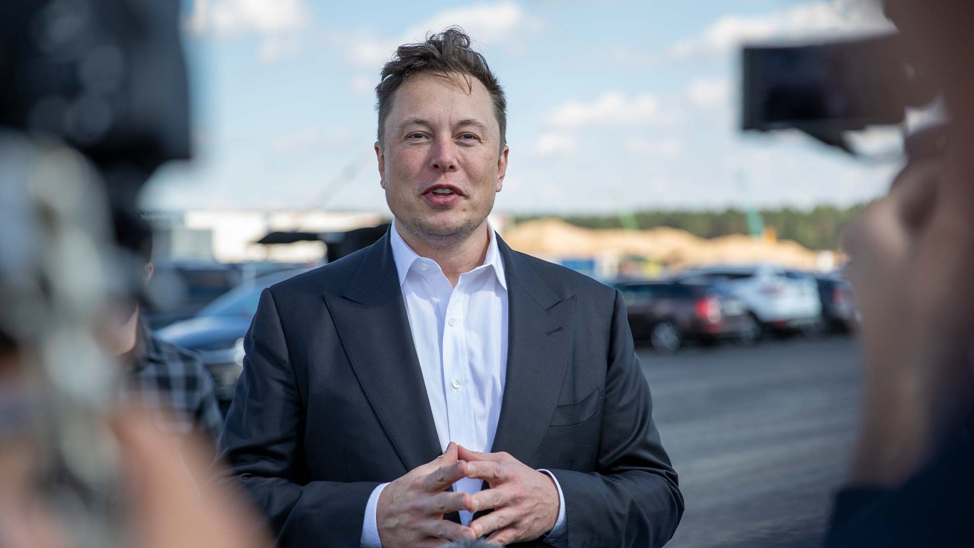 Elon Musk speaking to reporters in front of a parking lot