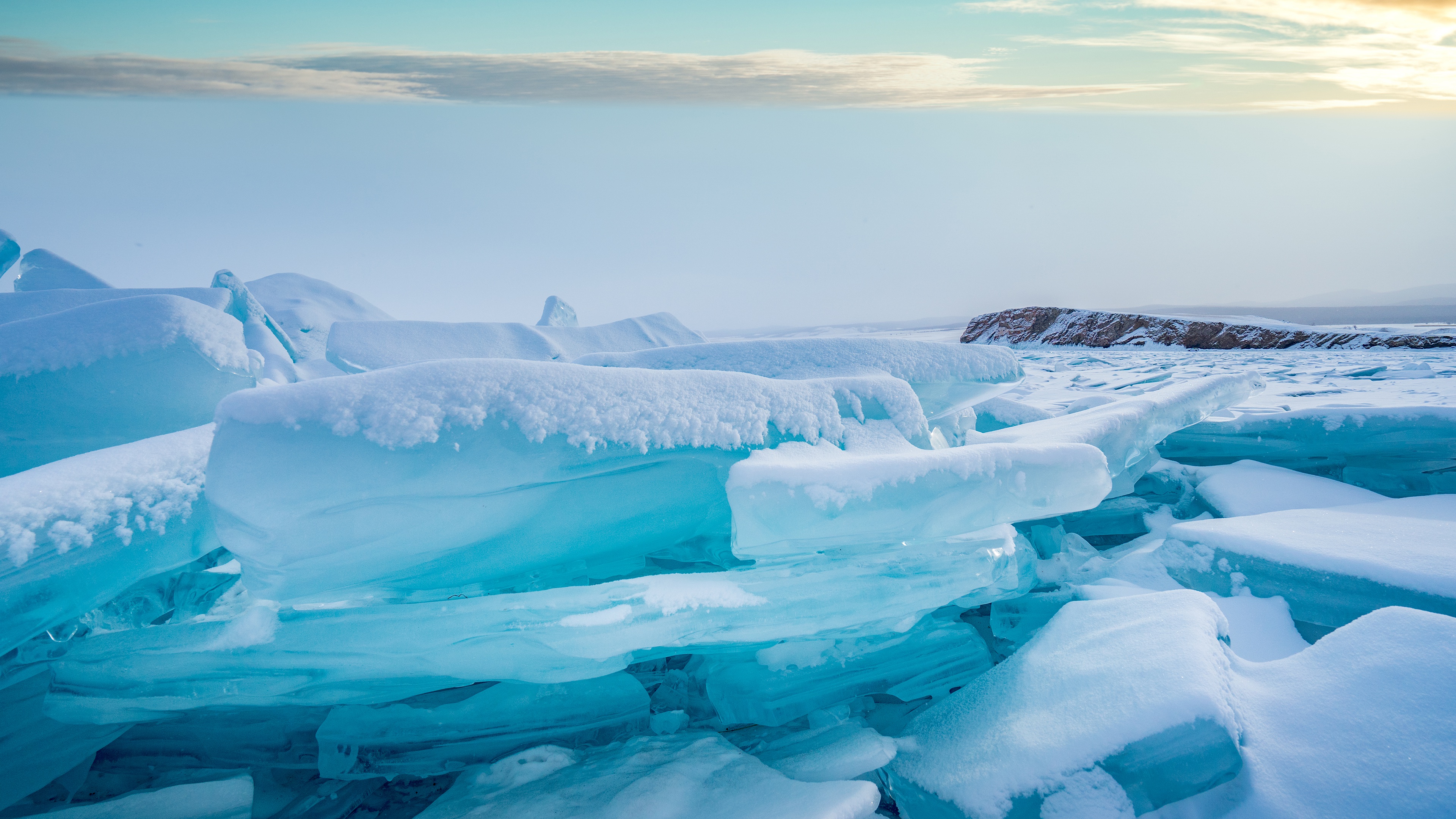 Turquoise ice formations on a frozen lake, dusted with snow, under a serene winter sky