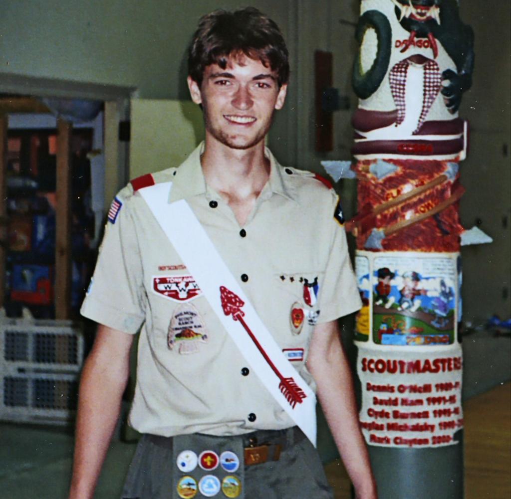 A young man in a Boy Scout uniform, possibly Ross Ulbricht, stands near a totem pole