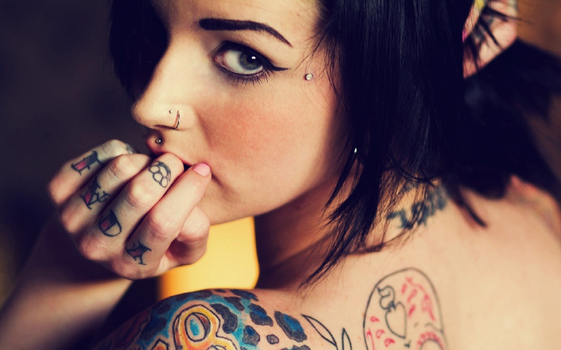 Close-up of a woman with various tattoos and piercings, including finger tattoos and a neck tattoo