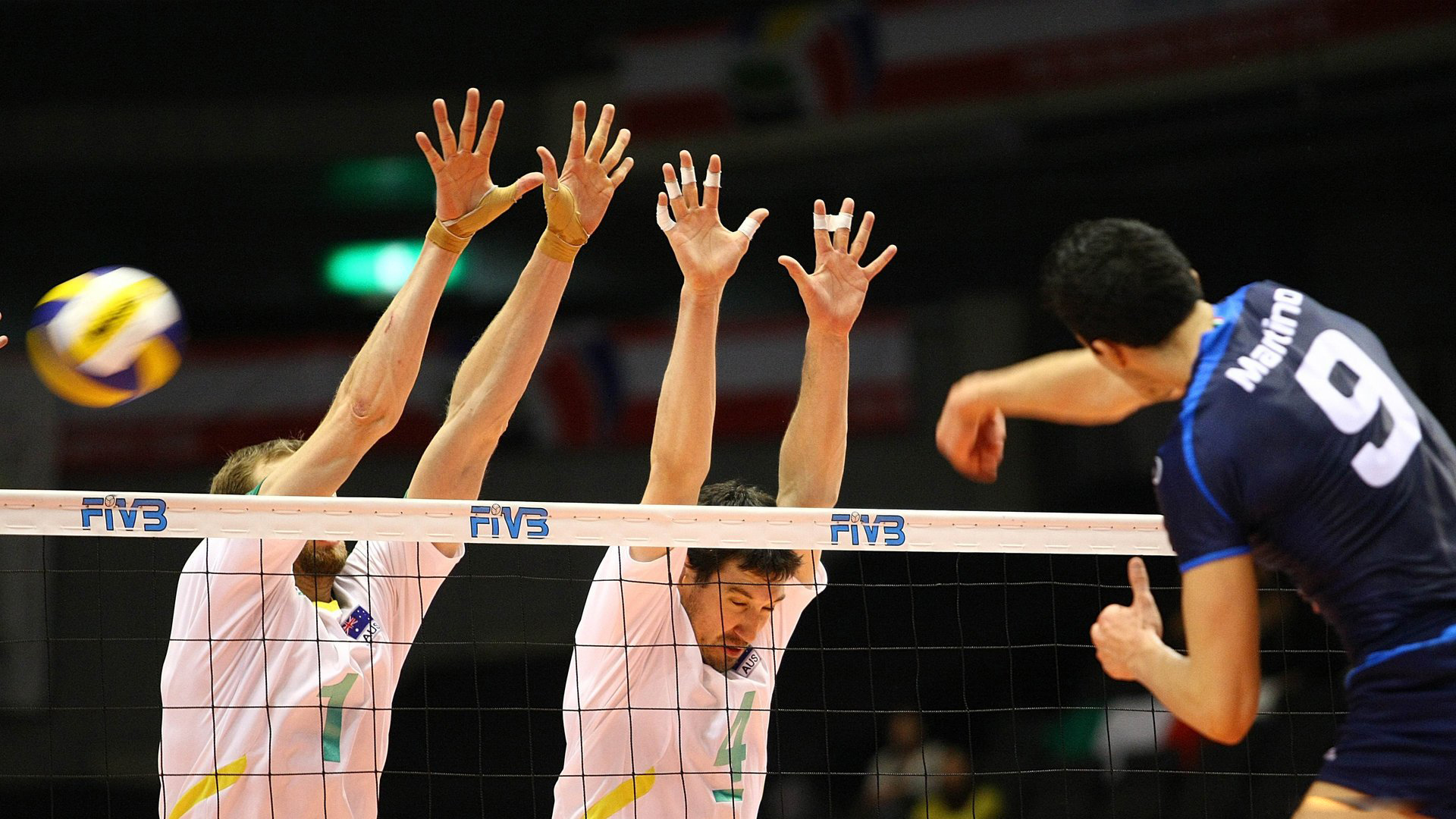 Volleyball players jumping up to the net to block the ball during a professional match