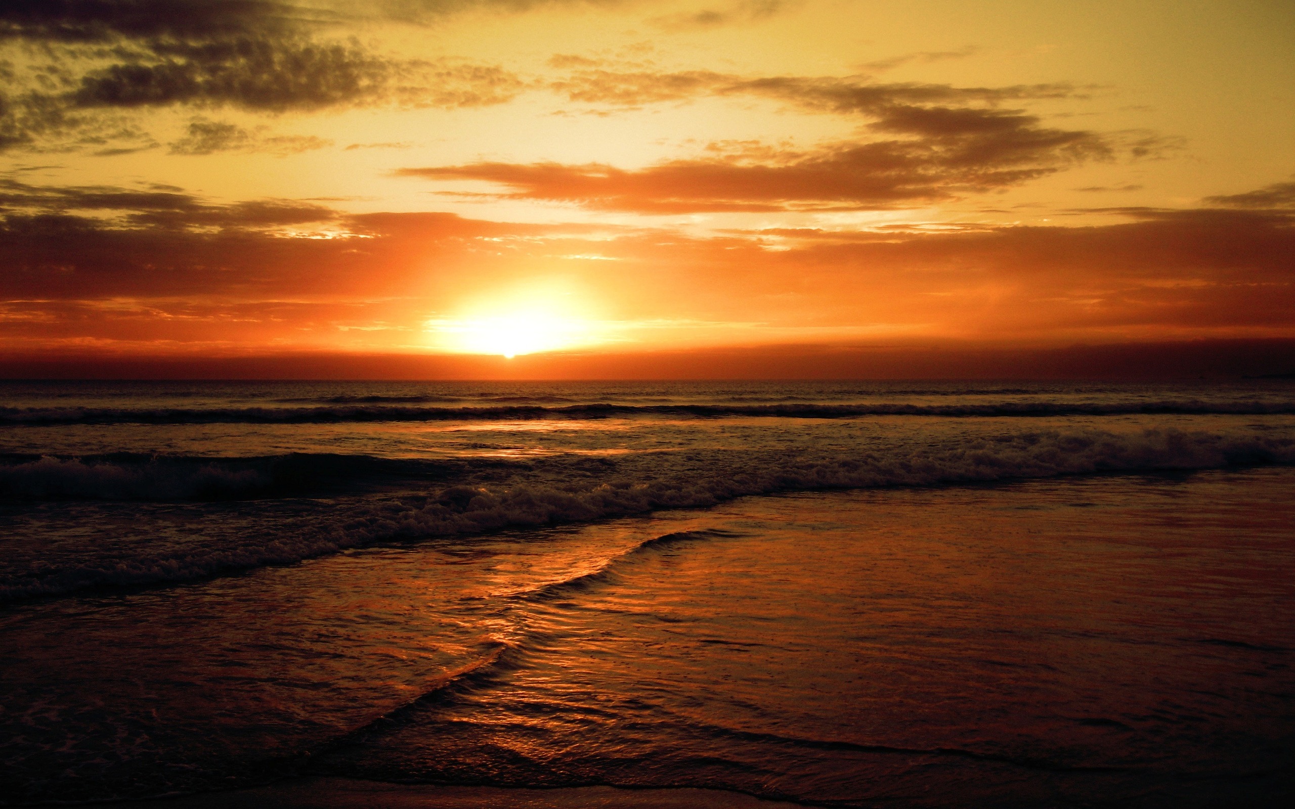 Fiery sunset over a tranquil ocean, casting warm golden hues across the waves and sky